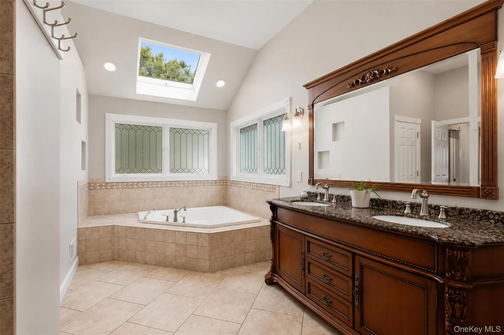 Bathroom featuring a built-in corner jet tub with tiled surround, a large skylight, vaulted ceiling, and recessed lighting Bathroom featuring a built-in corner jet tub with tiled surround, a large skylight, vaulted ceiling, and recessed lighting