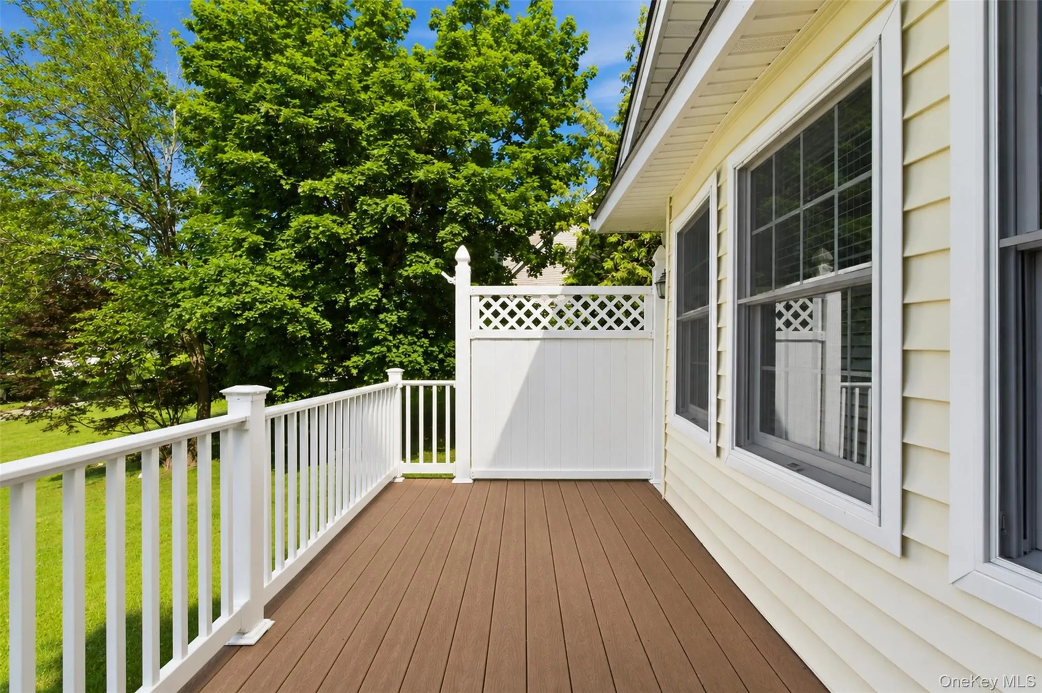 Exterior deck featuring composite wood-finish flooring, white railing, and white lattice privacy screen Exterior deck featuring composite wood-finish flooring, white railing, and white lattice privacy screen