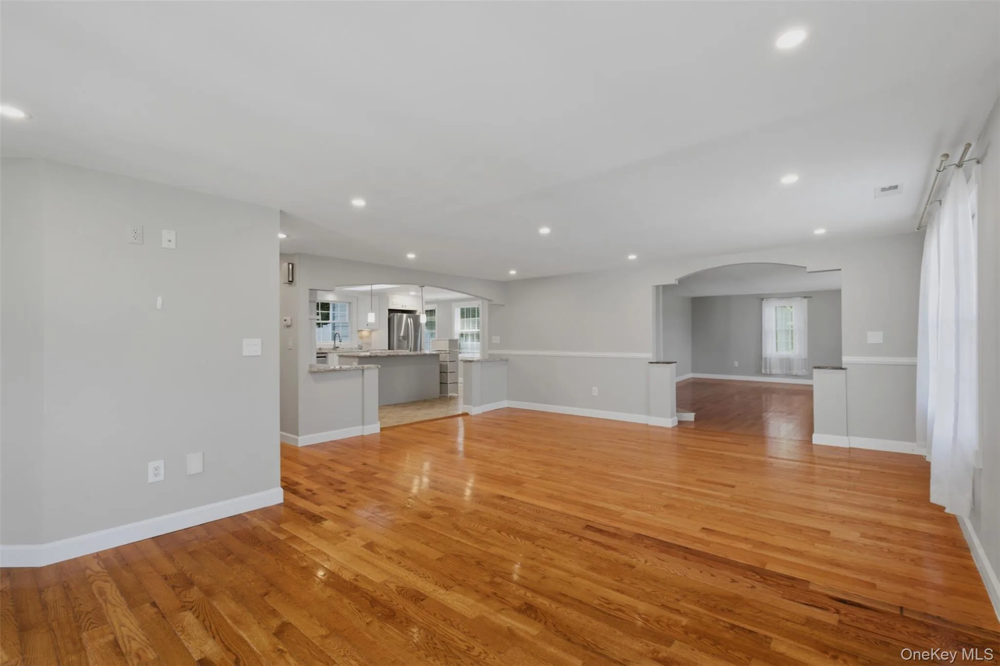 Spacious family room area featuring wood-finish flooring, recessed lighting, and a neutral color palette Spacious family room area featuring wood-finish flooring, recessed lighting, and a neutral color palette