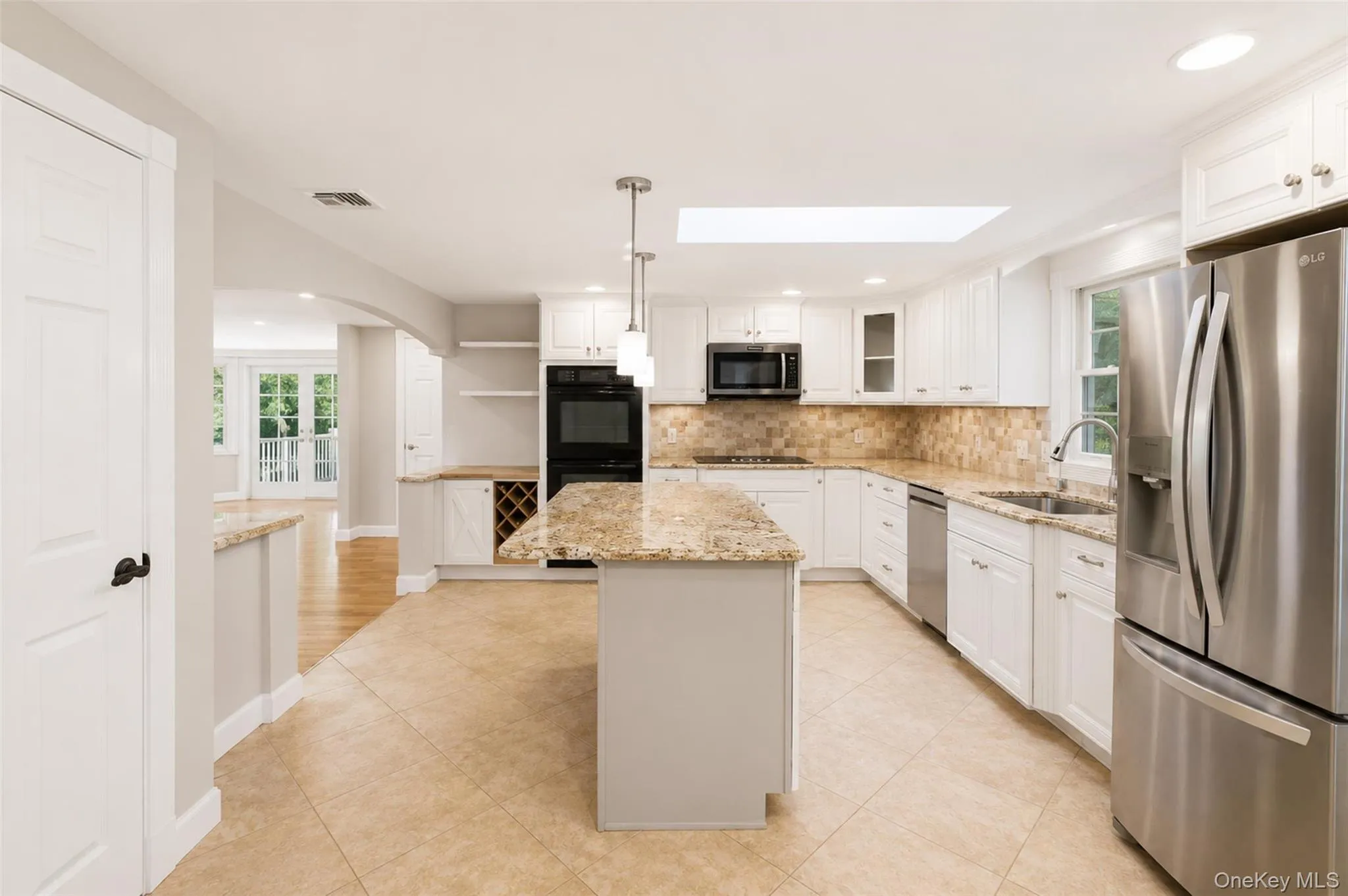 Spacious kitchen featuring an island with granite countertops, tile flooring, white cabinetry, stainless steel appliances, and a skylight Spacious kitchen featuring an island with granite countertops, tile flooring, white cabinetry, stainless steel appliances, and a skylight