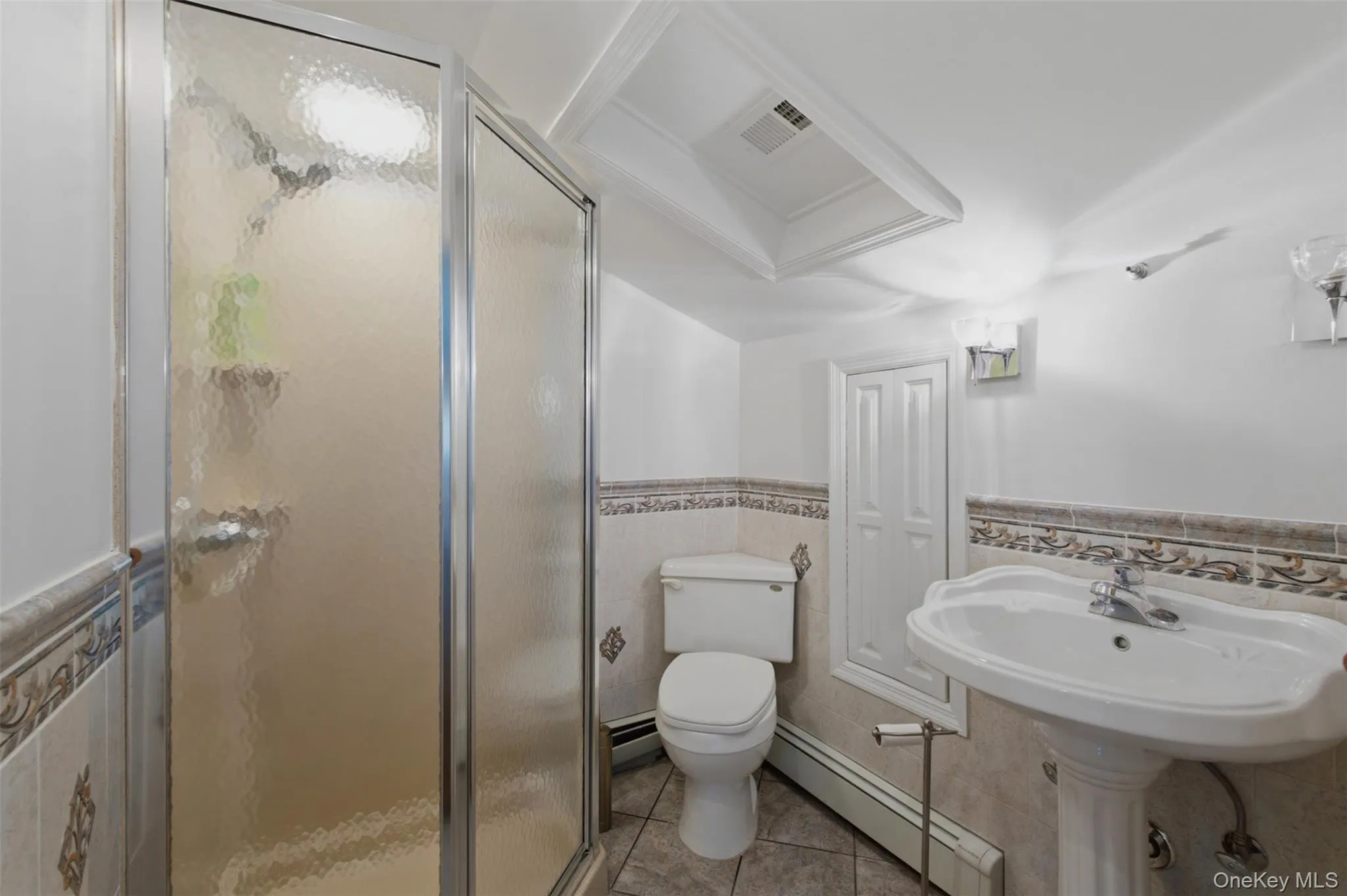 Full Bathroom in 3rd bedroom on the second level featuring a glass-enclosed shower, pedestal sink, ceramic tile flooring, and decorative wainscoting Full Bathroom in 3rd bedroom on the second level featuring a glass-enclosed shower, pedestal sink, ceramic tile flooring, and decorative wainscoting