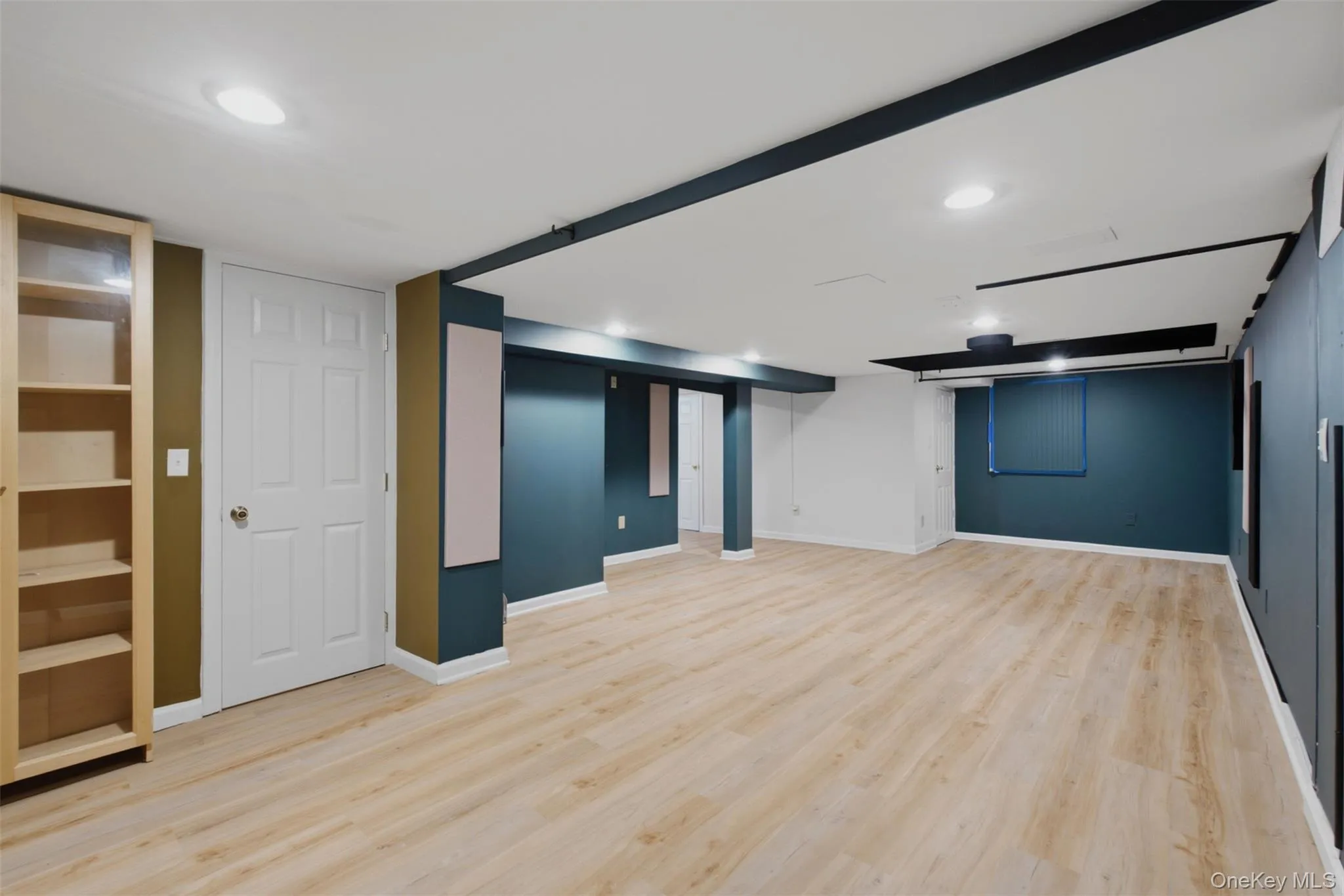 Spacious basement room featuring light wood-finish flooring, recessed lighting, accent walls, built-in shelving, and white trim Spacious basement room featuring light wood-finish flooring, recessed lighting, accent walls, built-in shelving, and white trim