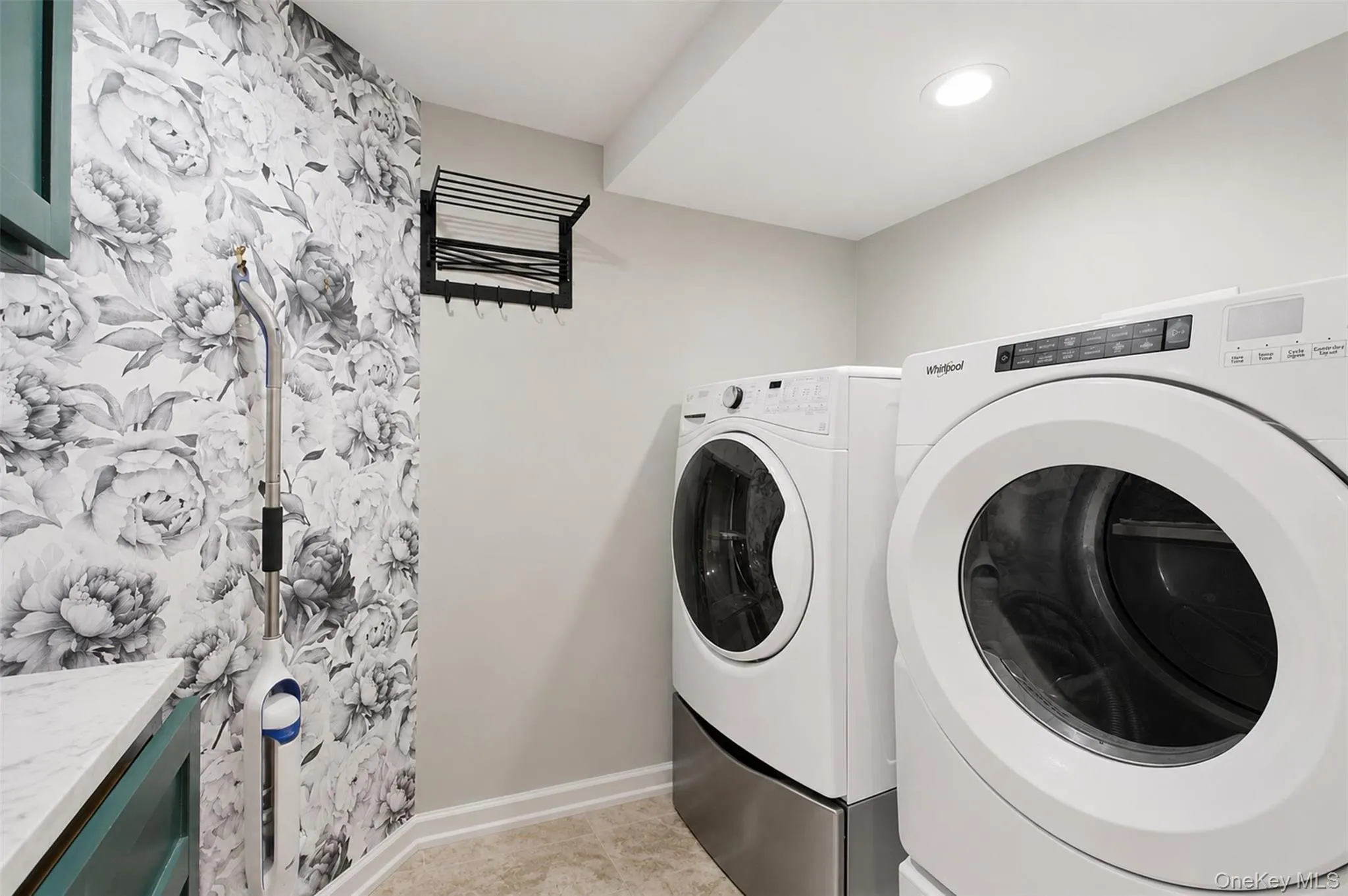 Dedicated laundry area featuring a front-load washer and dryer set on pedestals, recessed lighting, patterned accent wall, and a folding drying rack Dedicated laundry area featuring a front-load washer and dryer set on pedestals, recessed lighting, patterned accent wall, and a folding drying rack
