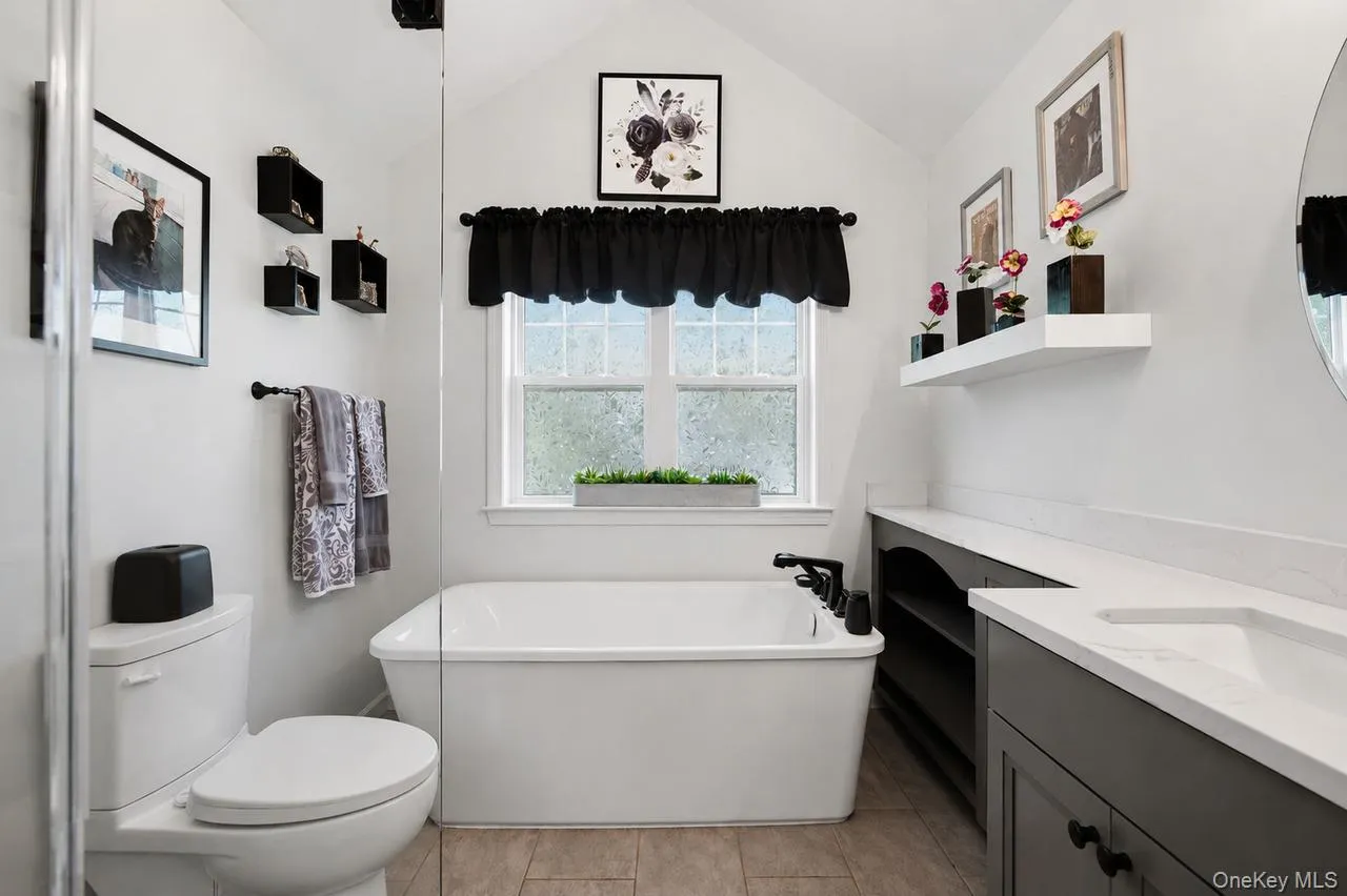 Bathroom featuring a contemporary freestanding tub, an integrated vanity with a single basin and dark cabinetry, and neutral tile flooring Bathroom featuring a contemporary freestanding tub, an integrated vanity with a single basin and dark cabinetry, and neutral tile flooring