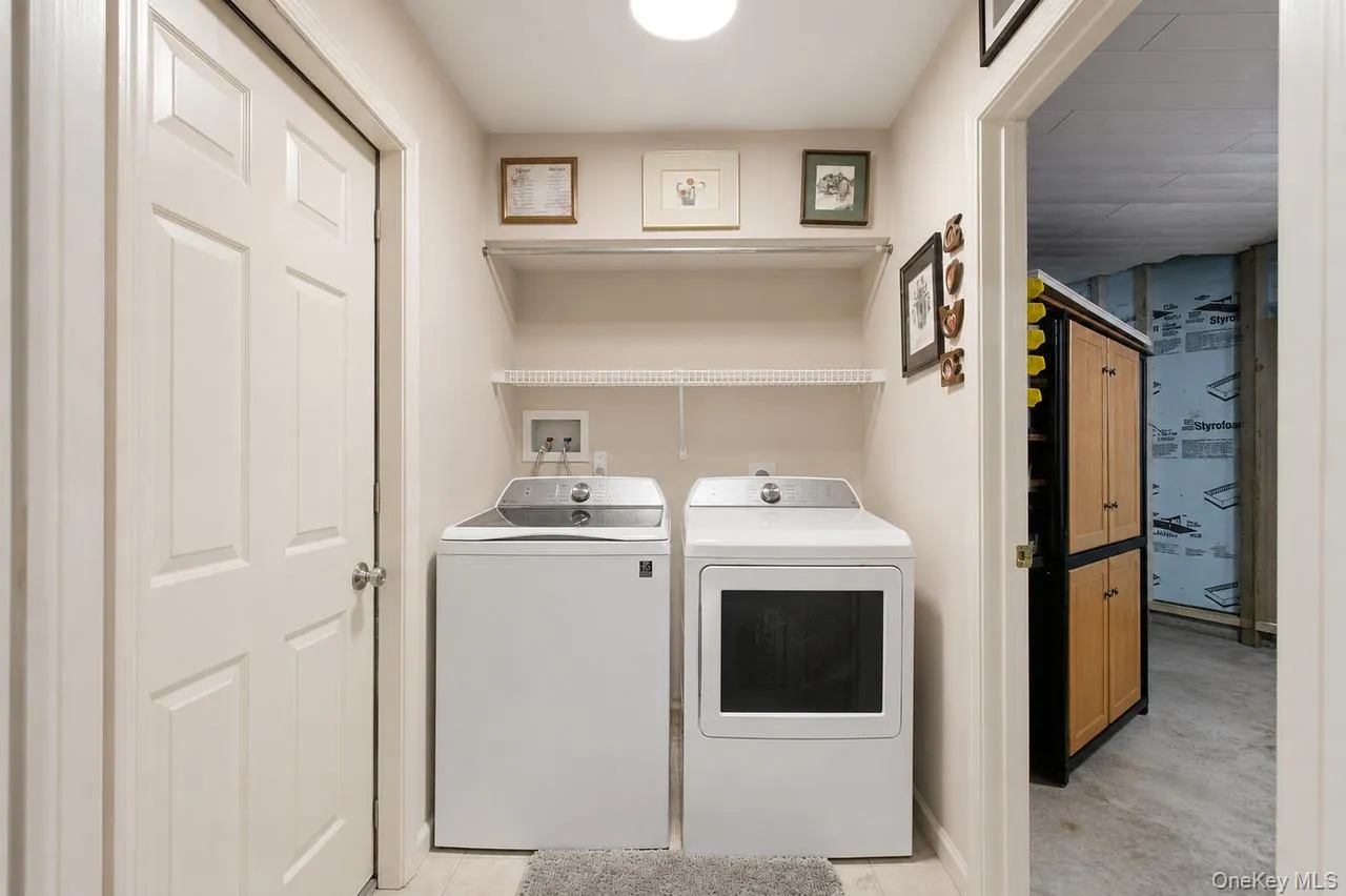 Dedicated laundry area featuring a white washer and dryer set, overhead wire shelving, and light-toned walls Dedicated laundry area featuring a white washer and dryer set, overhead wire shelving, and light-toned walls