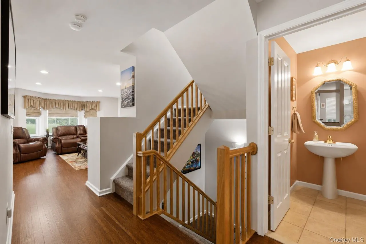 Staircase with light wood banister and carpeted treads, complemented by wood-finish flooring extending into a living area with recessed lighting Staircase with light wood banister and carpeted treads, complemented by wood-finish flooring extending into a living area with recessed lighting