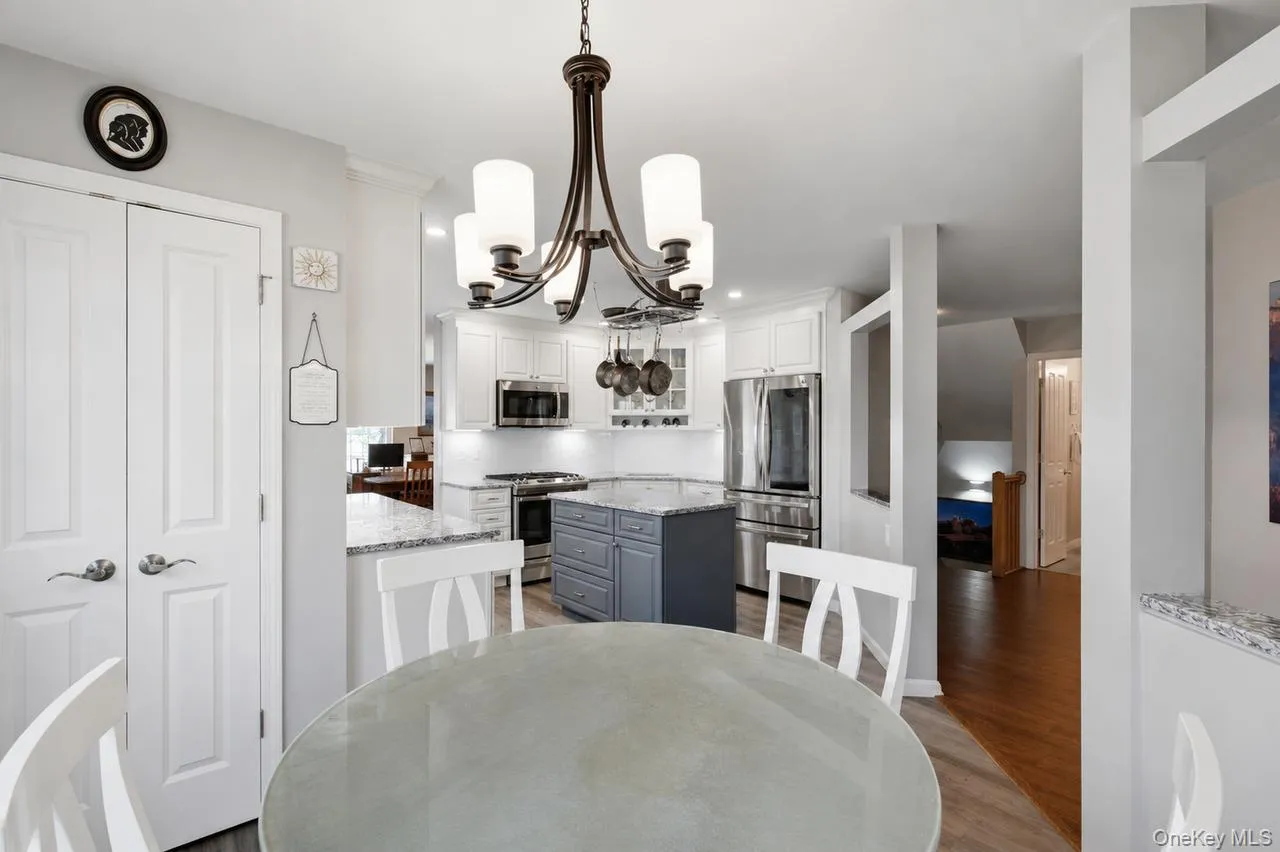 Kitchen featuring a central island with a contrasting base, white shaker-style cabinetry, stainless steel appliances, and light-toned countertops Kitchen featuring a central island with a contrasting base, white shaker-style cabinetry, stainless steel appliances, and light-toned countertops