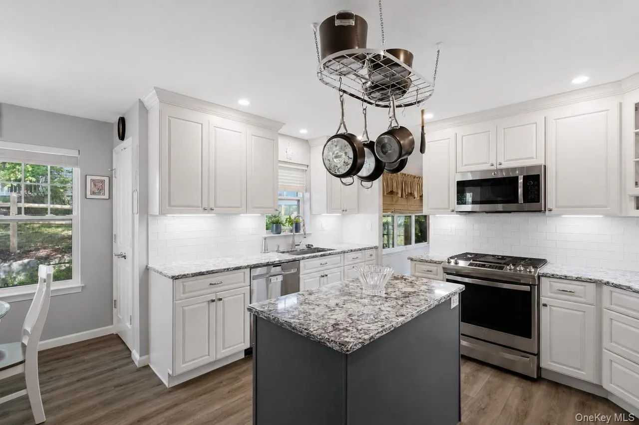 Kitchen featuring white shaker-style cabinetry, granite countertops, subway tile backsplash, a central island, and stainless steel appliances Kitchen featuring white shaker-style cabinetry, granite countertops, subway tile backsplash, a central island, and stainless steel appliances