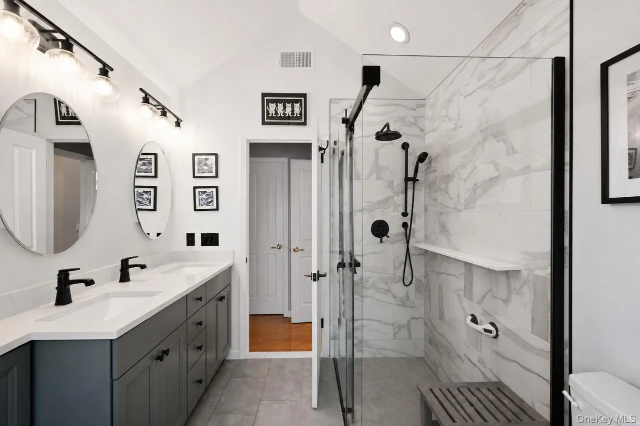 Vaulted ceiling bathroom featuring a dual vanity with quartz countertops, matte black plumbing fixtures, and a glass-enclosed shower with tile surround Vaulted ceiling bathroom featuring a dual vanity with quartz countertops, matte black plumbing fixtures, and a glass-enclosed shower with tile surround