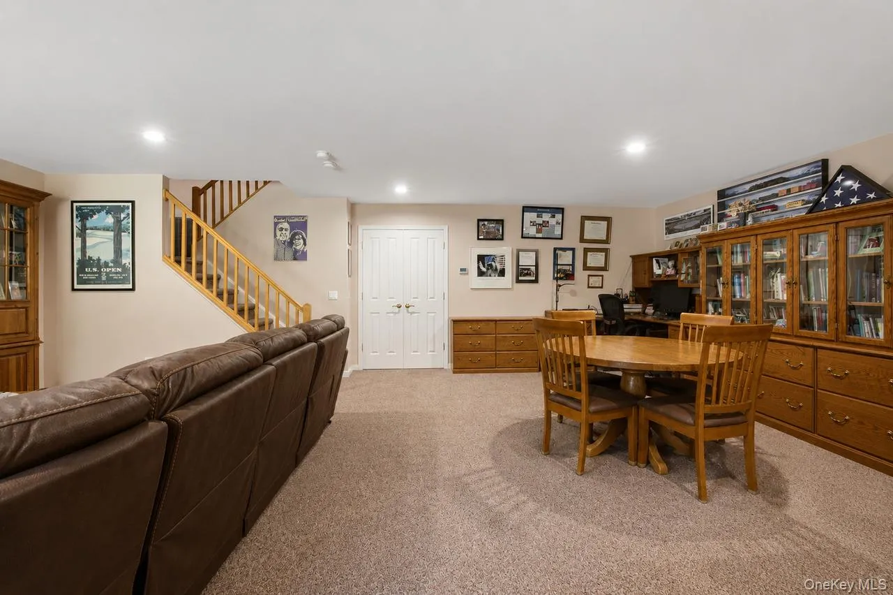 Spacious room with plush carpeting, recessed lighting, and a wood-finish staircase with open risers Spacious room with plush carpeting, recessed lighting, and a wood-finish staircase with open risers