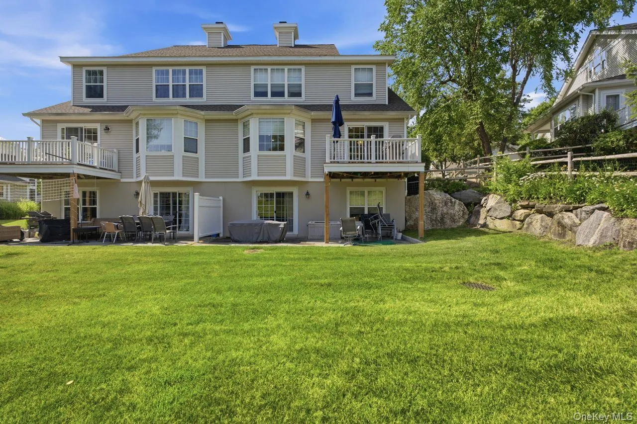 Spacious rear exterior featuring a large lawn, multiple decks, a ground-level patio, and natural rock landscaping Spacious rear exterior featuring a large lawn, multiple decks, a ground-level patio, and natural rock landscaping