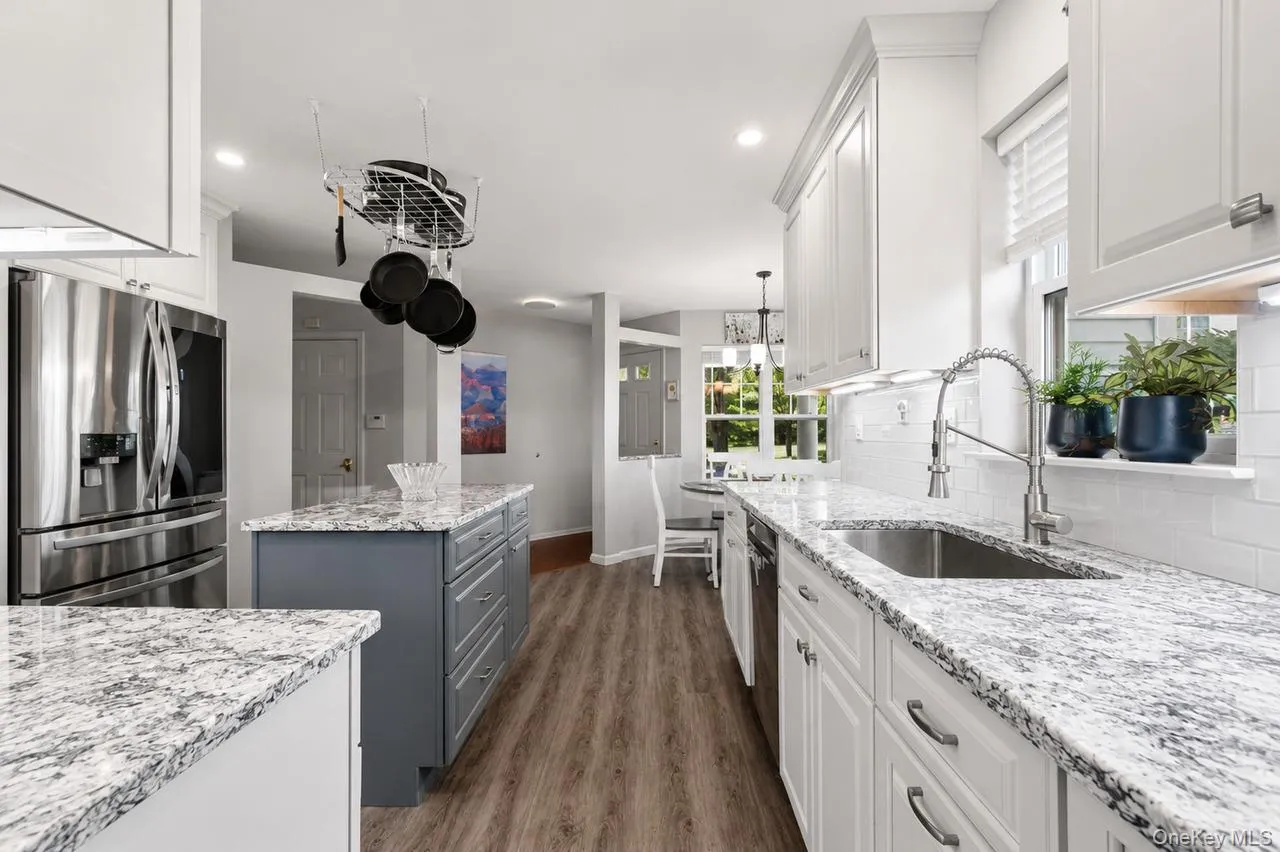 Spacious kitchen featuring white cabinetry, a large center island with gray cabinetry, stainless steel appliances, and wood-finish flooring Spacious kitchen featuring white cabinetry, a large center island with gray cabinetry, stainless steel appliances, and wood-finish flooring