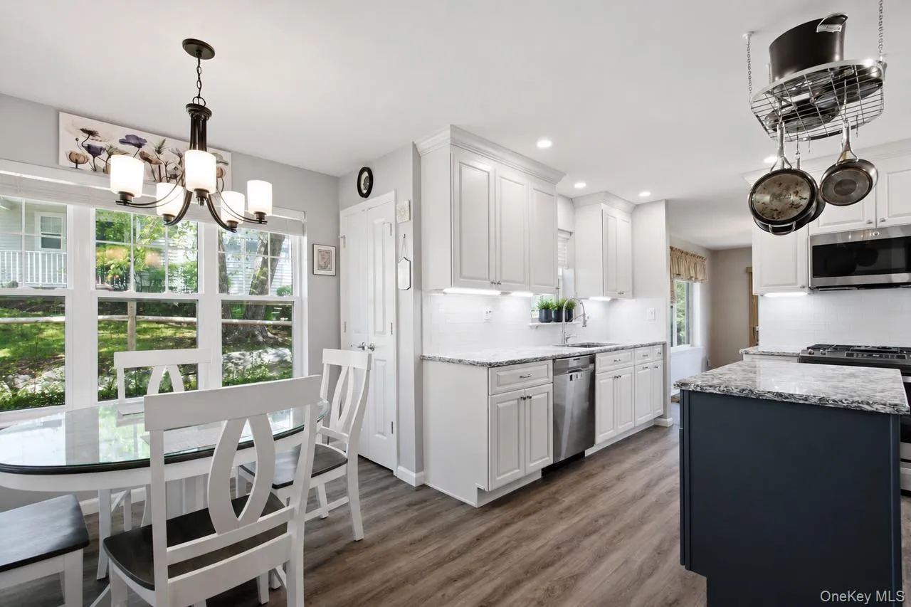 Open-concept kitchen featuring white shaker cabinetry, stainless steel appliances, granite countertops, and wood-finish flooring Open-concept kitchen featuring white shaker cabinetry, stainless steel appliances, granite countertops, and wood-finish flooring