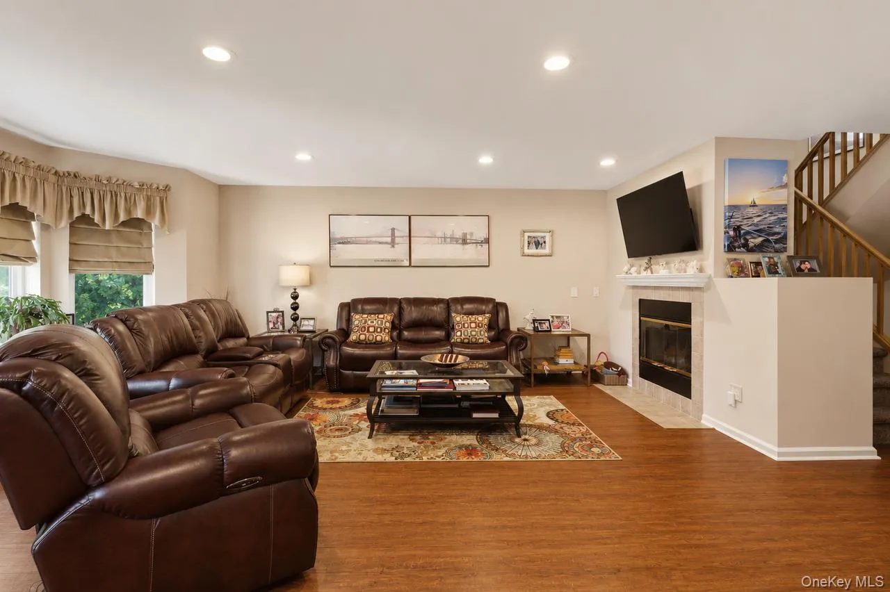 Spacious living area featuring wood-finish flooring, recessed lighting, and a fireplace with a light-toned tile surround and mantel Spacious living area featuring wood-finish flooring, recessed lighting, and a fireplace with a light-toned tile surround and mantel