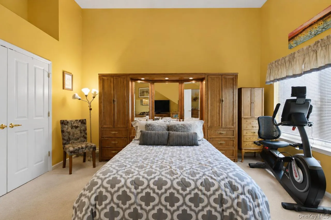 Spacious room featuring vaulted ceilings, light-toned carpeting, a large window with blinds, and white bi-fold closet doors Spacious room featuring vaulted ceilings, light-toned carpeting, a large window with blinds, and white bi-fold closet doors