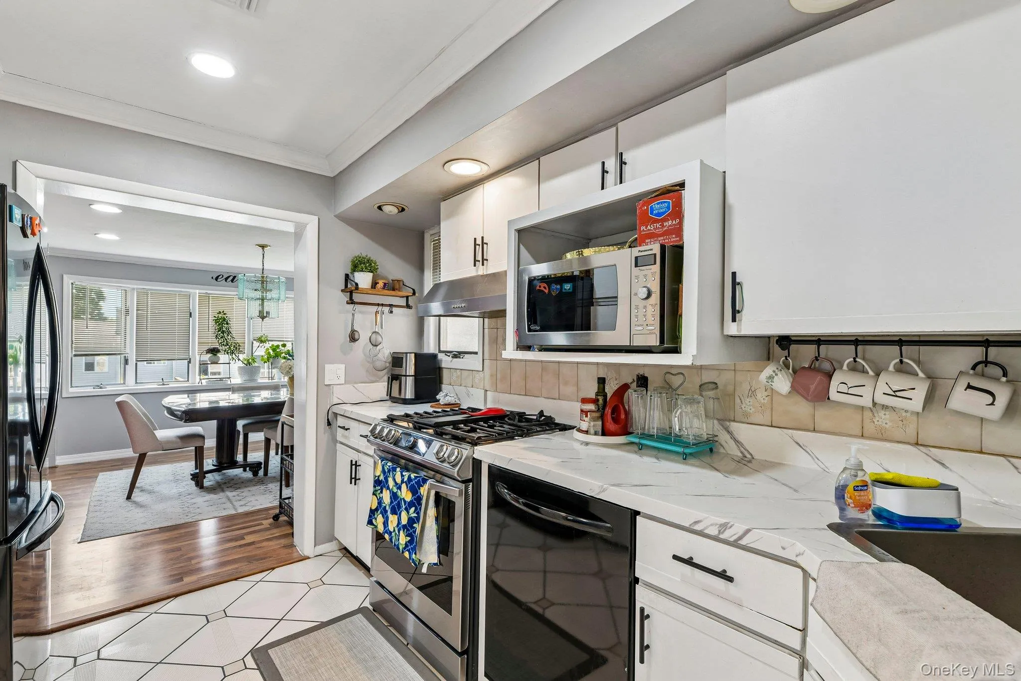Kitchen featuring white cabinetry, a gas range with a stainless steel vent hood, white countertops, and a tile backsplash Kitchen featuring white cabinetry, a gas range with a stainless steel vent hood, white countertops, and a tile backsplash