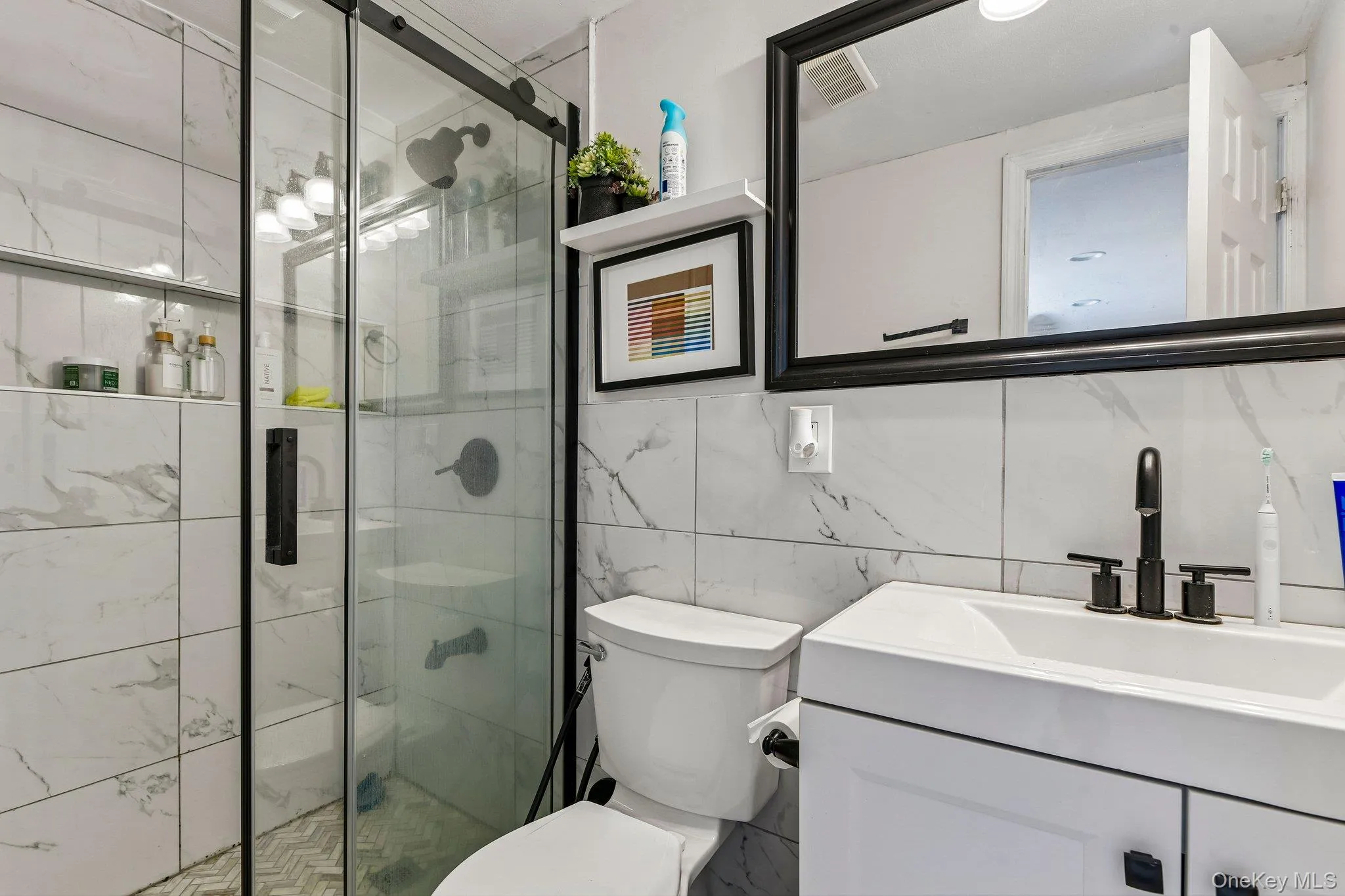 Bathroom featuring a glass-enclosed shower with black trim, a white vanity with black hardware, a rectangular sink with a matte black faucet, and a wall-mounted mirror with a black frame Bathroom featuring a glass-enclosed shower with black trim, a white vanity with black hardware, a rectangular sink with a matte black faucet, and a wall-mounted mirror with a black frame