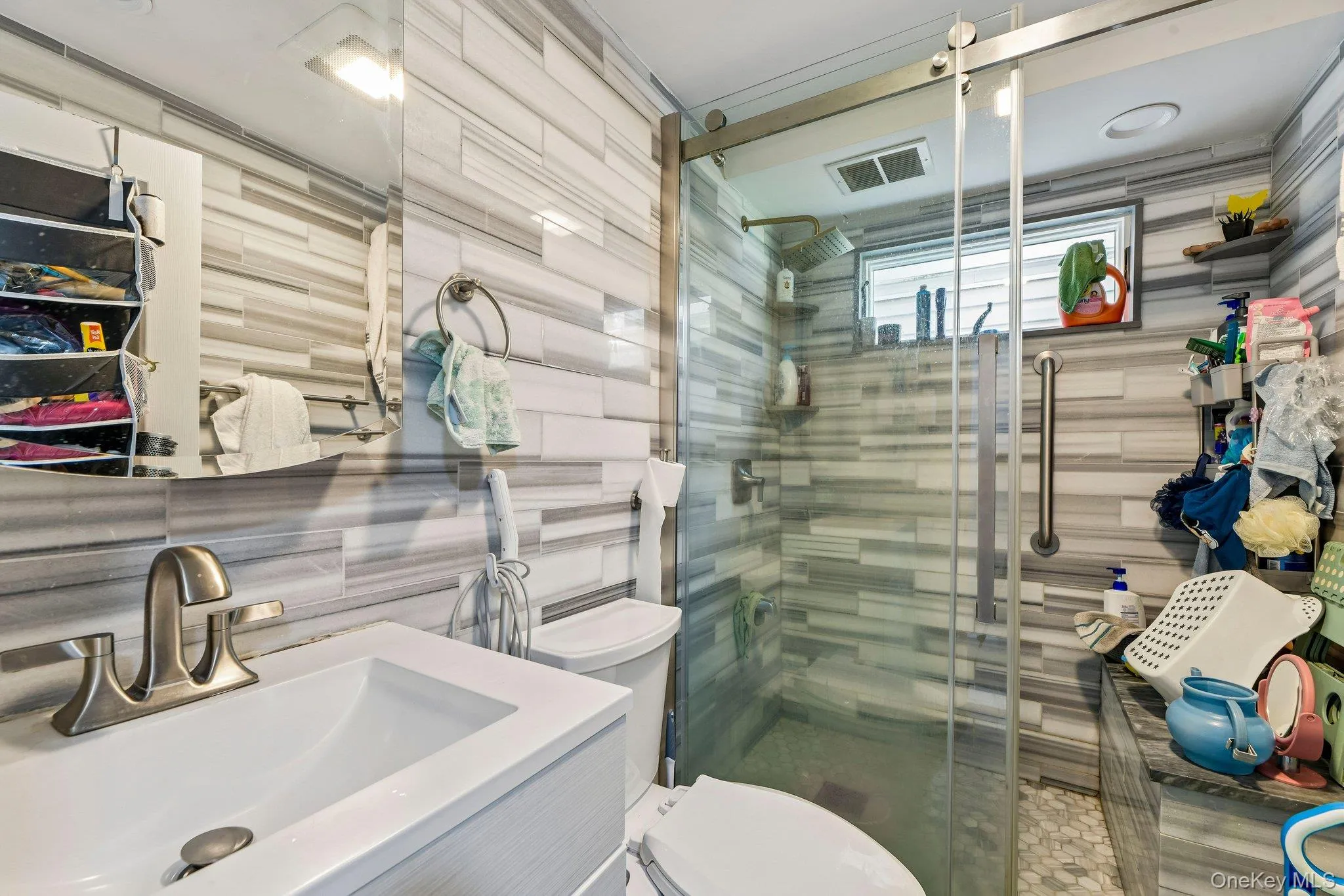 Modern bathroom featuring a glass-enclosed shower with sliding door, a white rectangular sink, brushed nickel faucet, and textured tile walls Modern bathroom featuring a glass-enclosed shower with sliding door, a white rectangular sink, brushed nickel faucet, and textured tile walls