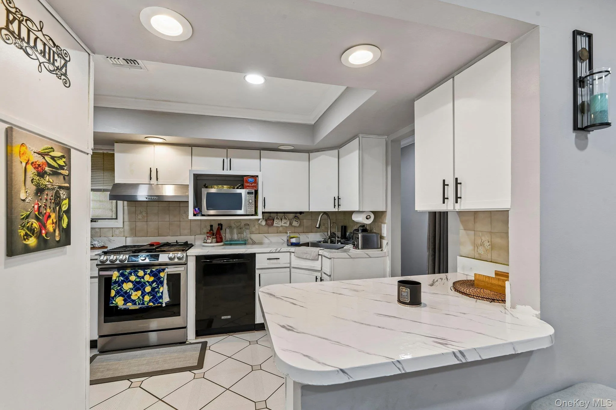 White cabinetry kitchen featuring a white and gray veined countertop peninsula, recessed lighting, stainless steel range with overhead ventilation, and a built-in microwave White cabinetry kitchen featuring a white and gray veined countertop peninsula, recessed lighting, stainless steel range with overhead ventilation, and a built-in microwave