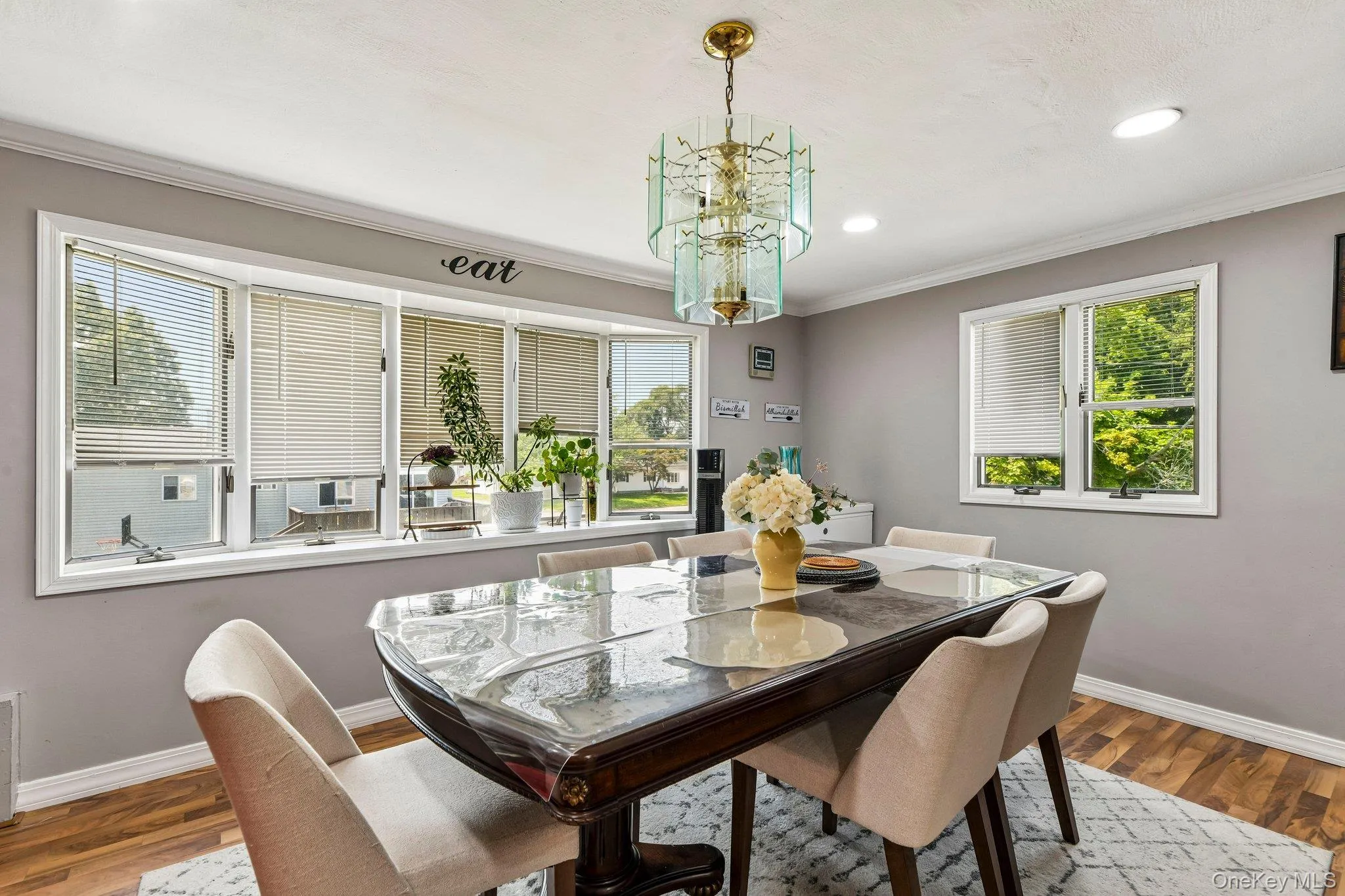 Dining area featuring a prominent bay window with blinds, wood-finish flooring, and a decorative chandelier Dining area featuring a prominent bay window with blinds, wood-finish flooring, and a decorative chandelier