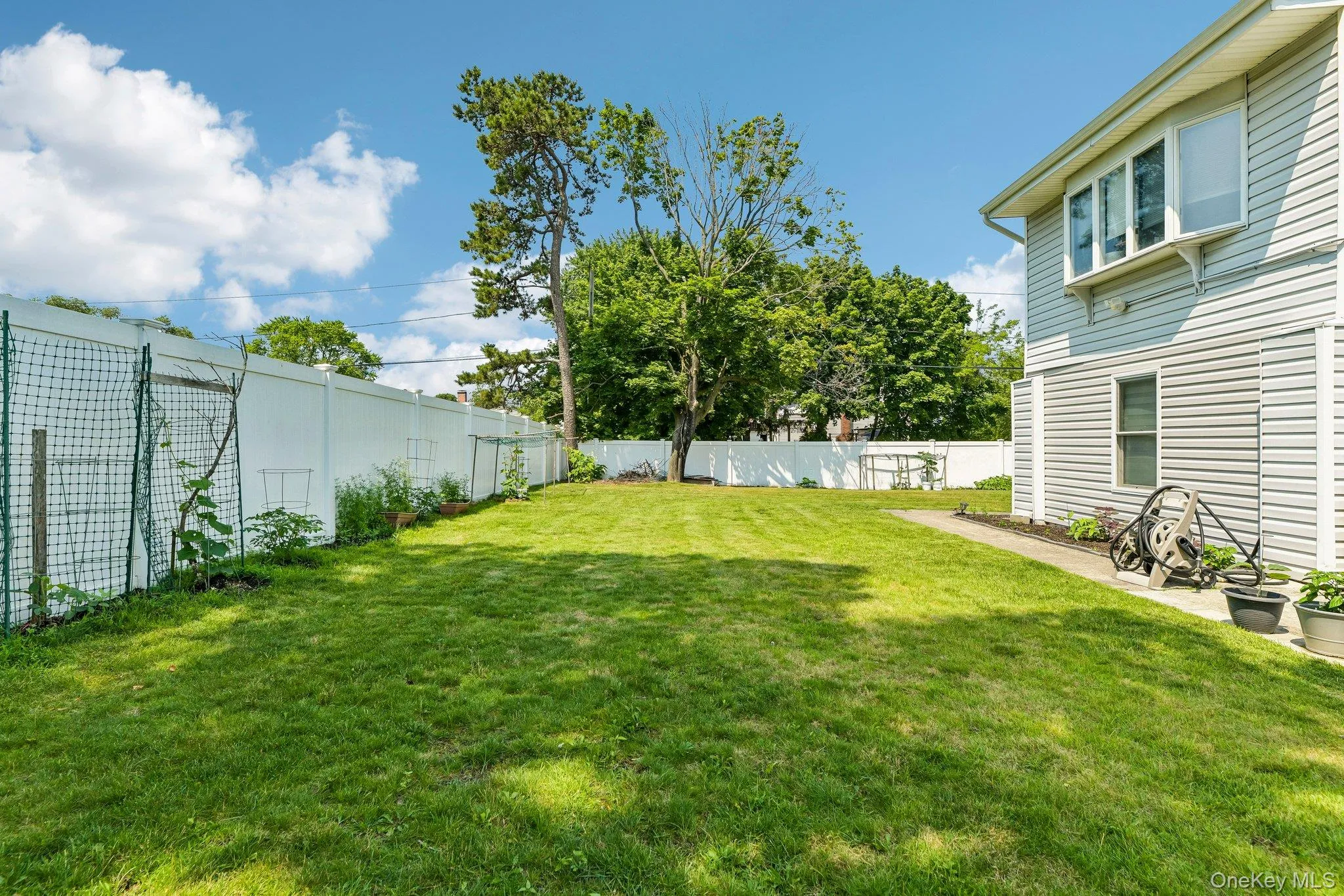 Expansive lawn area featuring a white privacy fence, mature trees, and a garden space Expansive lawn area featuring a white privacy fence, mature trees, and a garden space