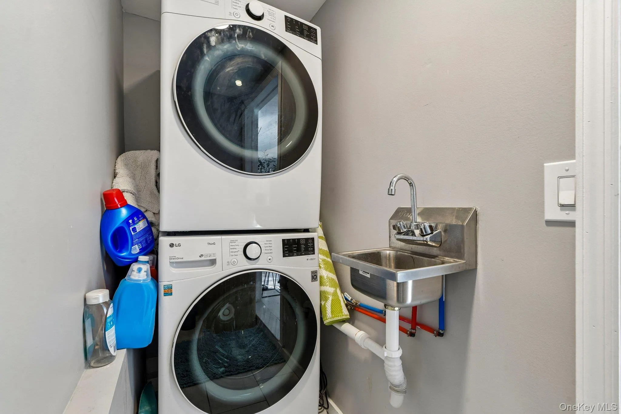 Dedicated laundry area featuring a stacked washer and dryer unit, a wall-mounted utility sink with exposed plumbing, and light gray wall finishes Dedicated laundry area featuring a stacked washer and dryer unit, a wall-mounted utility sink with exposed plumbing, and light gray wall finishes