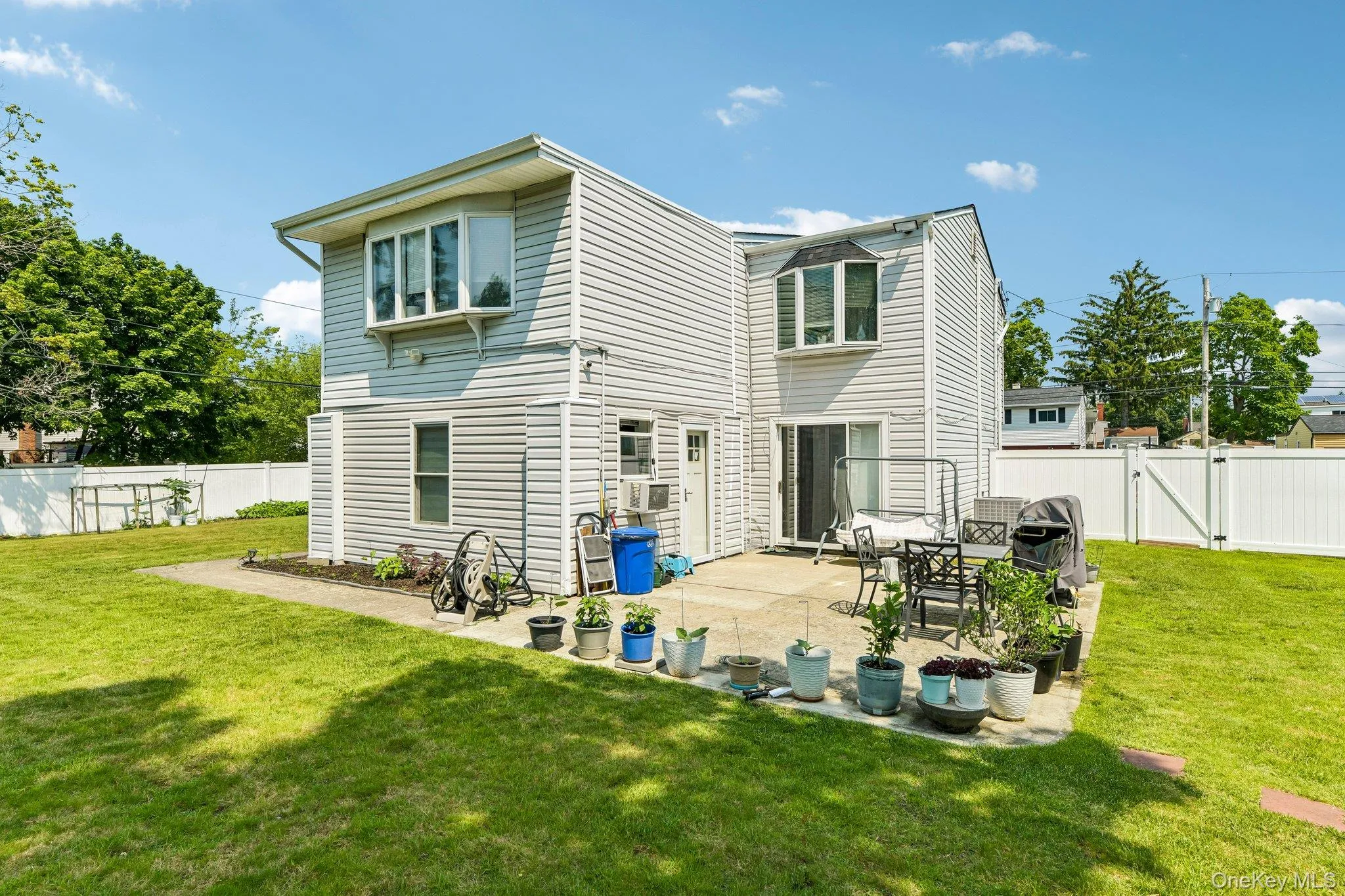 Rear exterior with light gray siding, featuring a ground-level concrete patio, bay windows on the second story, a sliding glass door, and white privacy fencing Rear exterior with light gray siding, featuring a ground-level concrete patio, bay windows on the second story, a sliding glass door, and white privacy fencing