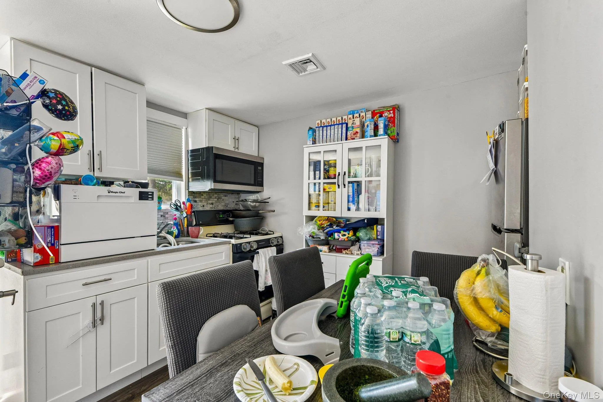 Kitchen featuring white shaker cabinetry, light-toned countertops, a stainless steel over-the-range microwave, and a gas range Kitchen featuring white shaker cabinetry, light-toned countertops, a stainless steel over-the-range microwave, and a gas range