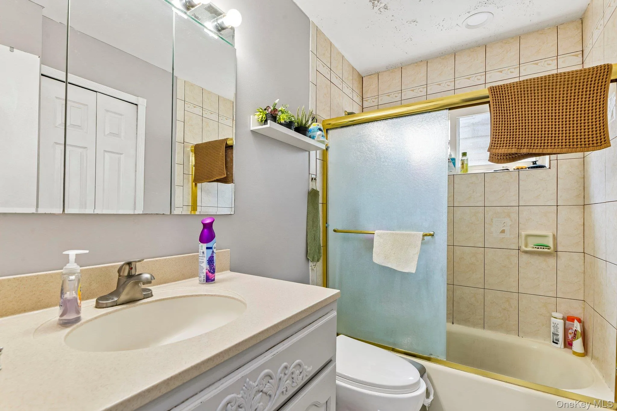 Bathroom featuring a built-in bathtub with sliding frosted glass doors, light-toned square wall tiles, and a vanity with an integrated sink and light countertop Bathroom featuring a built-in bathtub with sliding frosted glass doors, light-toned square wall tiles, and a vanity with an integrated sink and light countertop