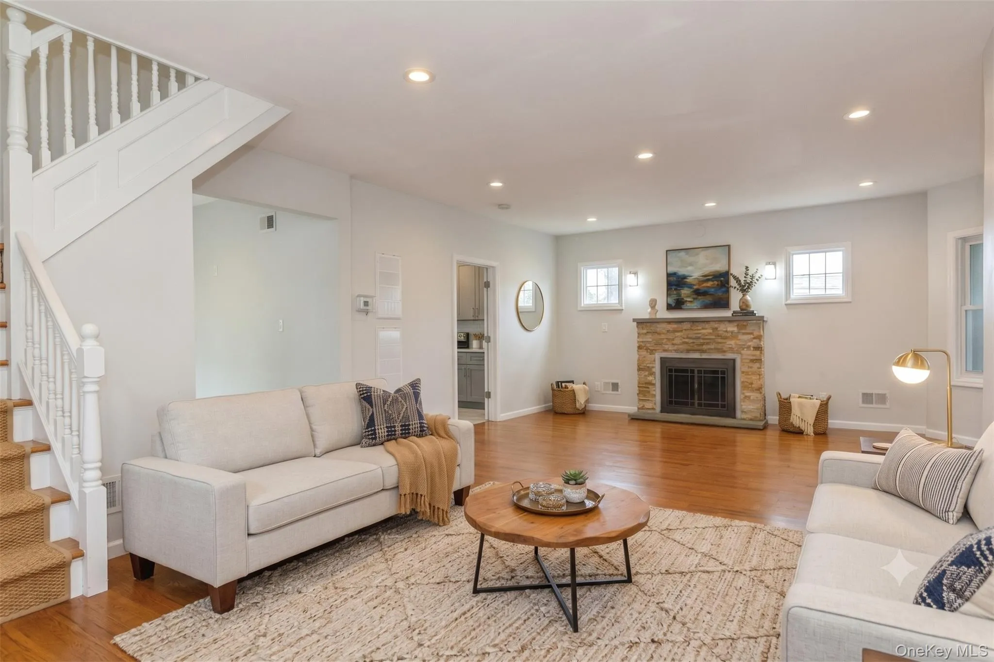 Spacious living area featuring polished wood flooring, a stone-clad fireplace, and recessed lighting Spacious living area featuring polished wood flooring, a stone-clad fireplace, and recessed lighting
