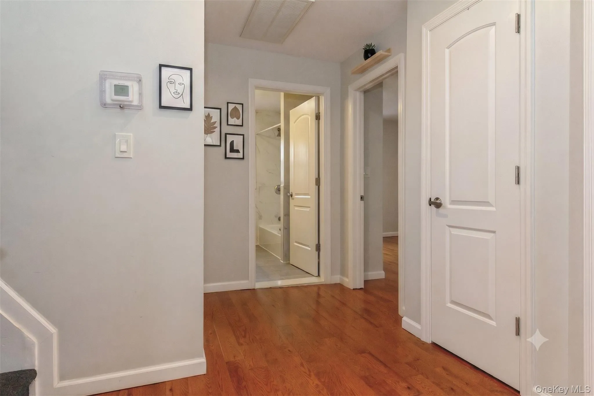 Hardwood-style flooring throughout hallway featuring light gray wall paint, white trim, and white paneled doors with arch details Hardwood-style flooring throughout hallway featuring light gray wall paint, white trim, and white paneled doors with arch details
