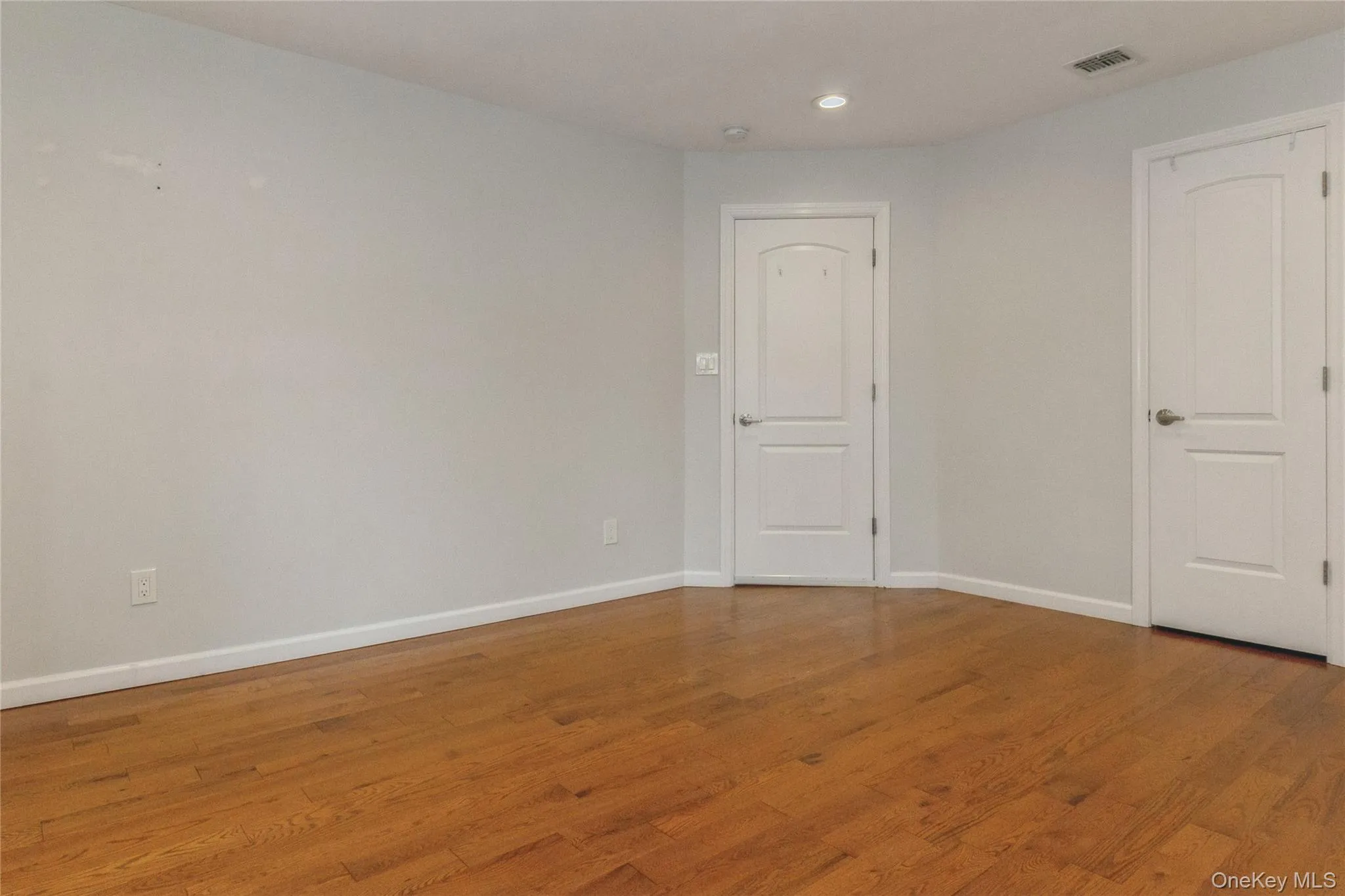 Interior room featuring wood-finish flooring, light-toned walls, and two white paneled closet doors Interior room featuring wood-finish flooring, light-toned walls, and two white paneled closet doors