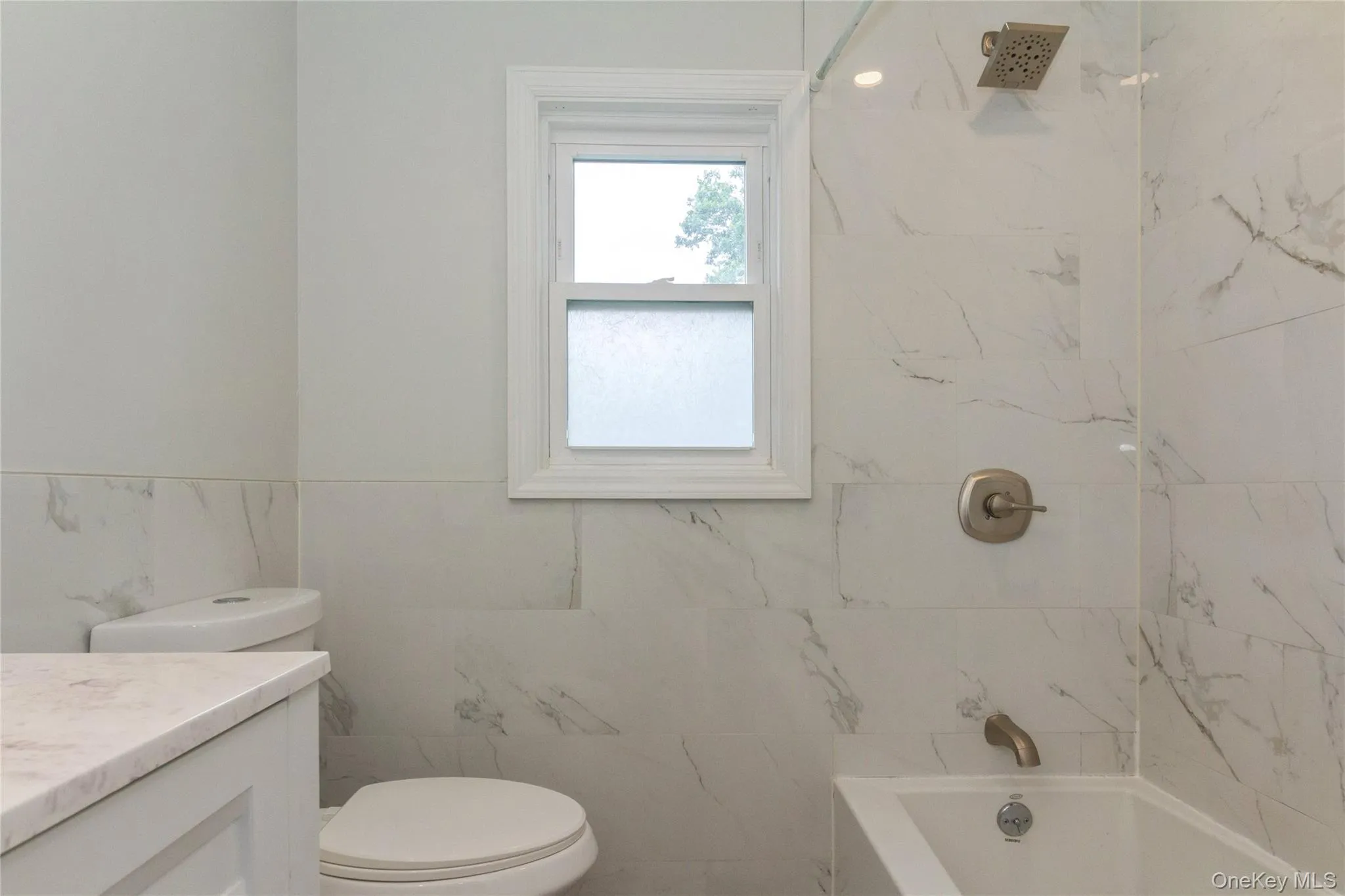 Bathroom featuring large format marble-look wall tiles, a built-in bathtub with brushed nickel fixtures, and a white framed window Bathroom featuring large format marble-look wall tiles, a built-in bathtub with brushed nickel fixtures, and a white framed window