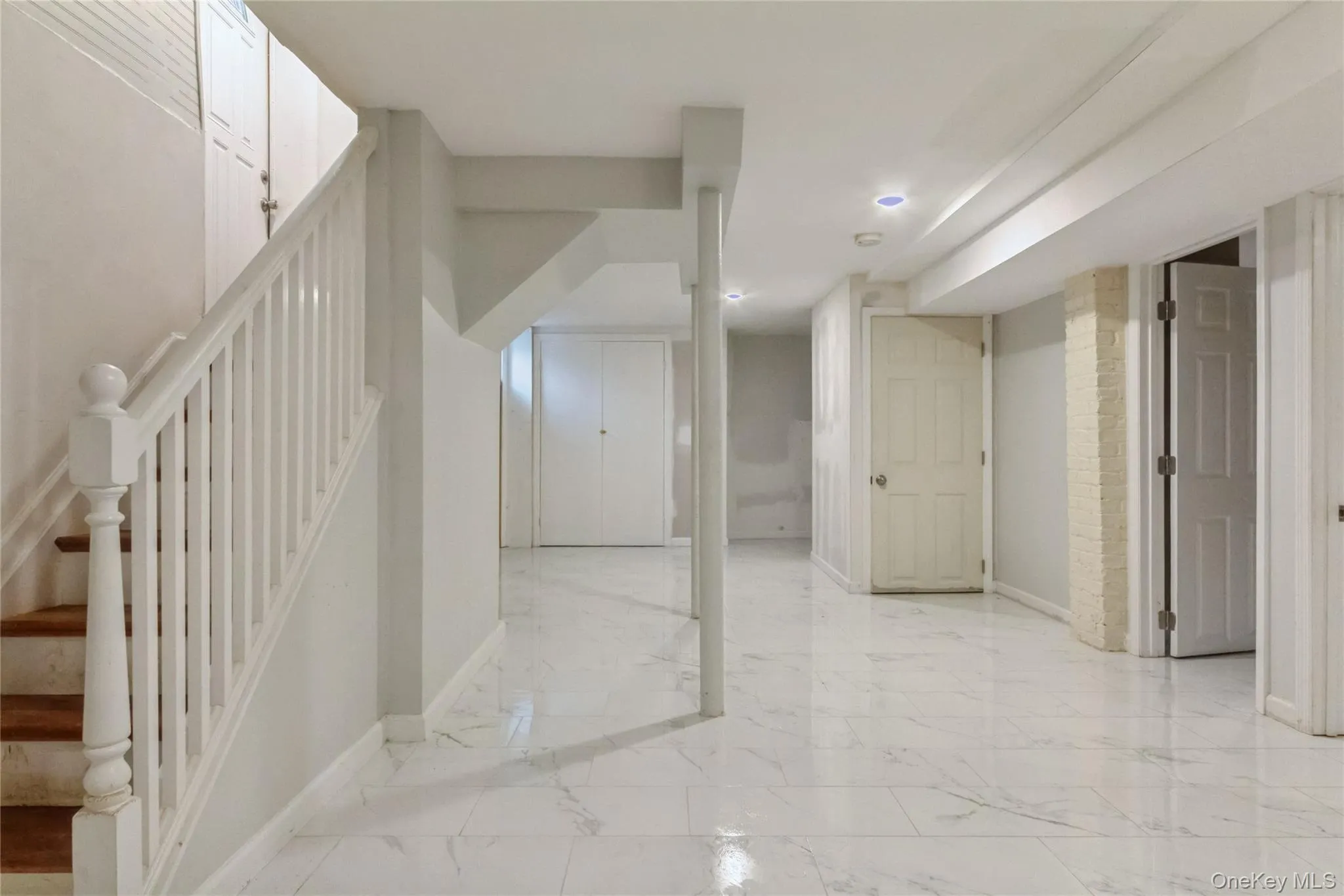 Finished basement space featuring white marble-look tile flooring, recessed ceiling lighting, a white painted staircase with wood treads, and multiple white paneled doors Finished basement space featuring white marble-look tile flooring, recessed ceiling lighting, a white painted staircase with wood treads, and multiple white paneled doors