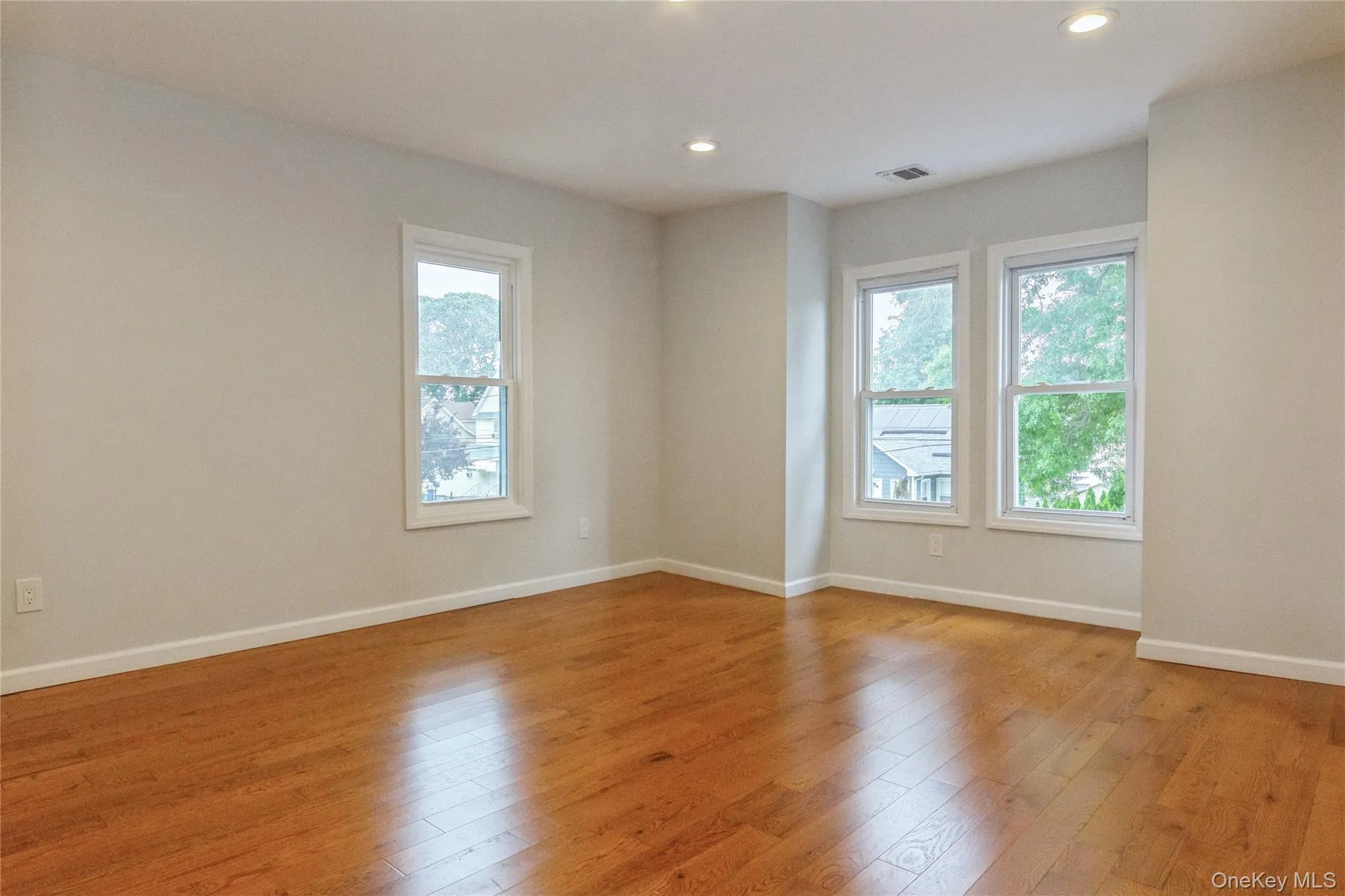 Spacious bedroom featuring wood-finish flooring, recessed lighting, and multiple windows Spacious bedroom featuring wood-finish flooring, recessed lighting, and multiple windows
