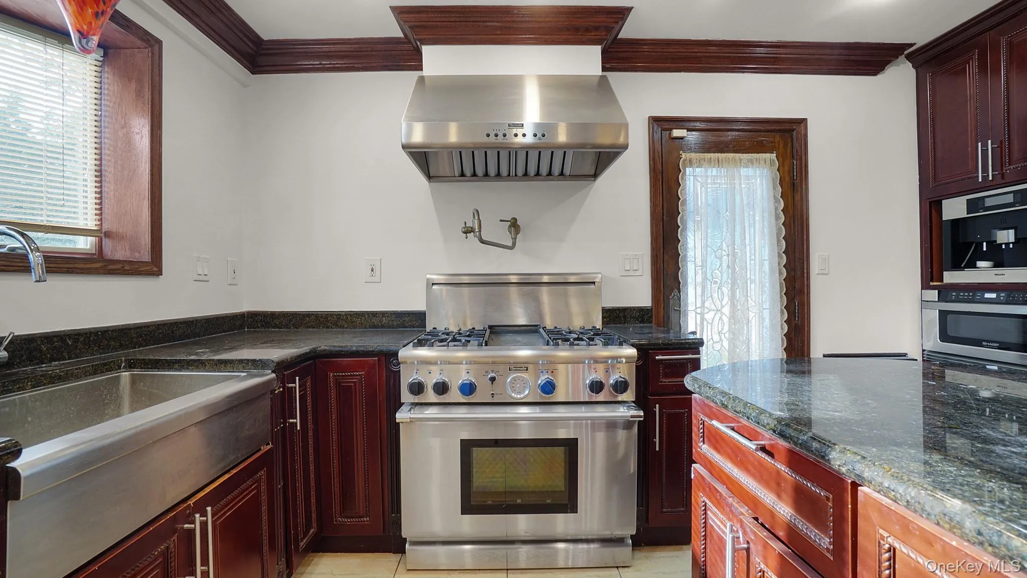 Kitchen featuring a stainless steel professional-grade range with a substantial range hood, dark wood cabinetry, and dark speckled countertops Kitchen featuring a stainless steel professional-grade range with a substantial range hood, dark wood cabinetry, and dark speckled countertops