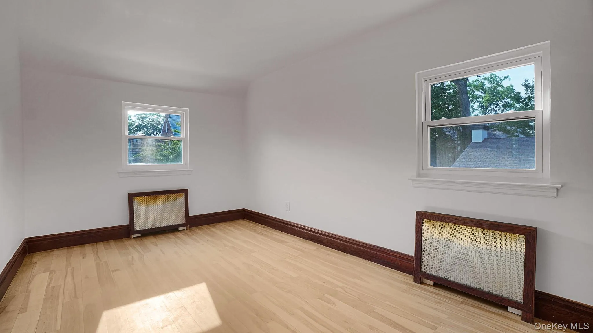 Hardwood flooring throughout, complemented by white walls, dark wood baseboards, and two windows with white trim Hardwood flooring throughout, complemented by white walls, dark wood baseboards, and two windows with white trim