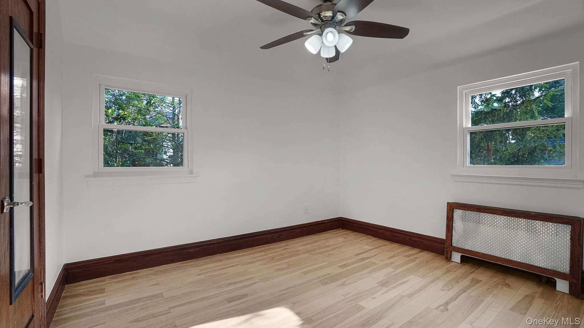 Bright interior room featuring wood-finish flooring, white walls, and dark wood trim Bright interior room featuring wood-finish flooring, white walls, and dark wood trim