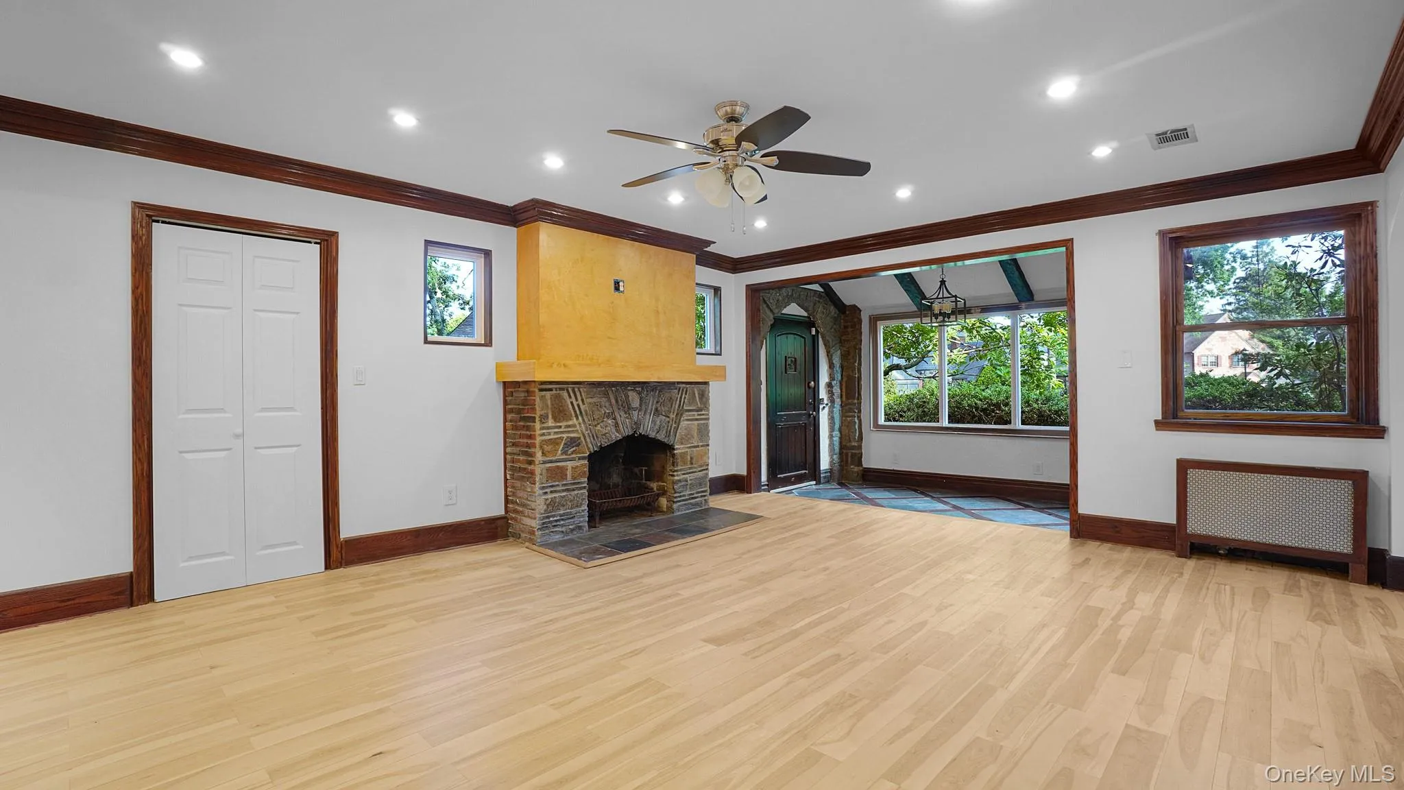 Spacious room featuring wood-finish flooring, a stone fireplace with a textured mantel, recessed lighting, and dark wood trim Spacious room featuring wood-finish flooring, a stone fireplace with a textured mantel, recessed lighting, and dark wood trim