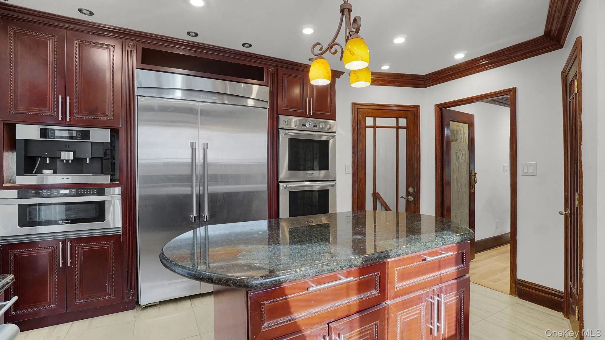 Kitchen featuring a central island with a granite countertop, built-in stainless steel appliances, dark wood cabinetry, crown molding, and recessed lighting Kitchen featuring a central island with a granite countertop, built-in stainless steel appliances, dark wood cabinetry, crown molding, and recessed lighting