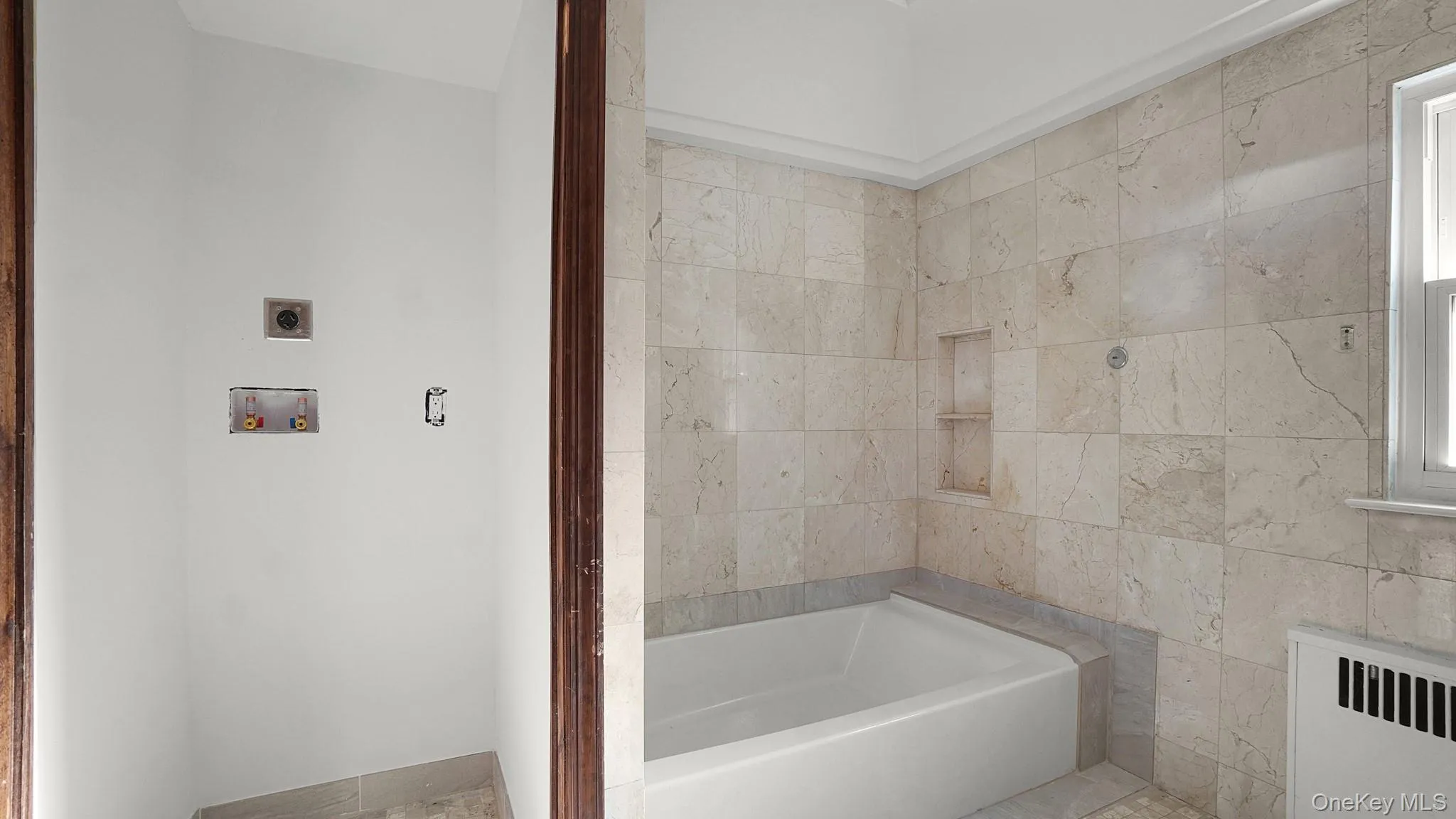 Bathroom featuring a built-in tub, extensive stone tiling, a window, and a wall niche Bathroom featuring a built-in tub, extensive stone tiling, a window, and a wall niche