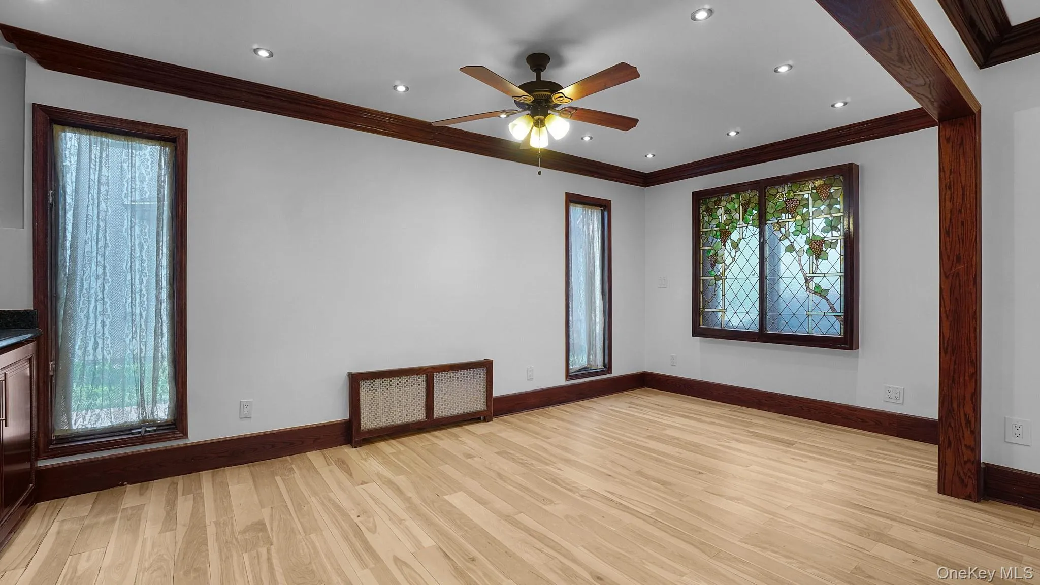 Spacious room with wood-finish flooring, dark wood trim, recessed lighting, and a ceiling fan Spacious room with wood-finish flooring, dark wood trim, recessed lighting, and a ceiling fan