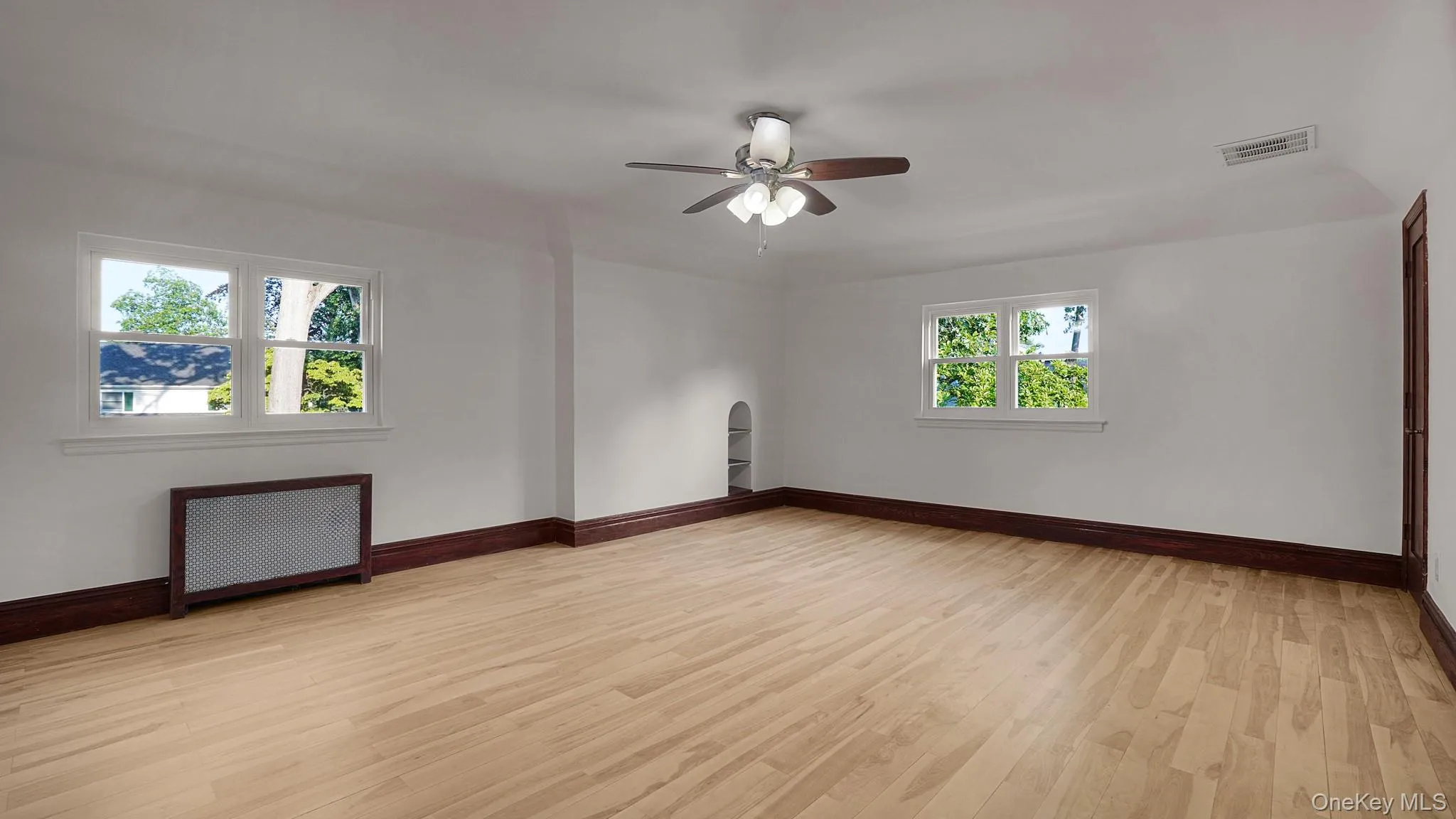 Spacious room featuring wood-finish flooring, white walls, and dark wood trim Spacious room featuring wood-finish flooring, white walls, and dark wood trim