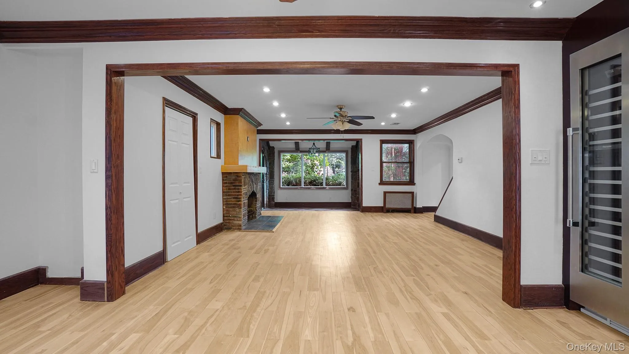 Expansive interior with light wood-finish flooring throughout, featuring dark wood trim, recessed lighting, and a stone fireplace with a contrasting mantel Expansive interior with light wood-finish flooring throughout, featuring dark wood trim, recessed lighting, and a stone fireplace with a contrasting mantel