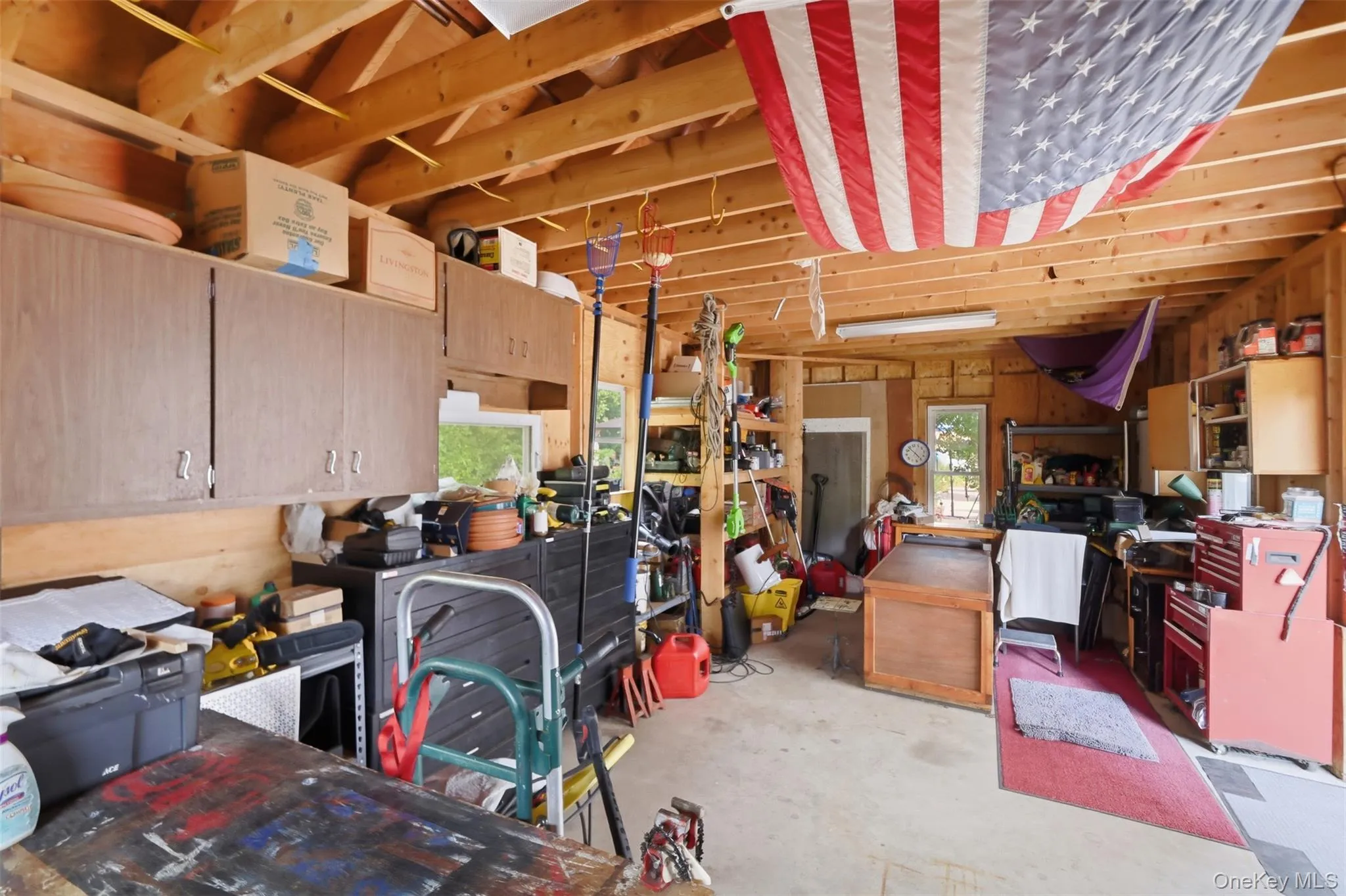 Expansive garage space featuring exposed wood beam ceilings, wood-paneled walls, built-in cabinetry, and a concrete floor Expansive garage space featuring exposed wood beam ceilings, wood-paneled walls, built-in cabinetry, and a concrete floor