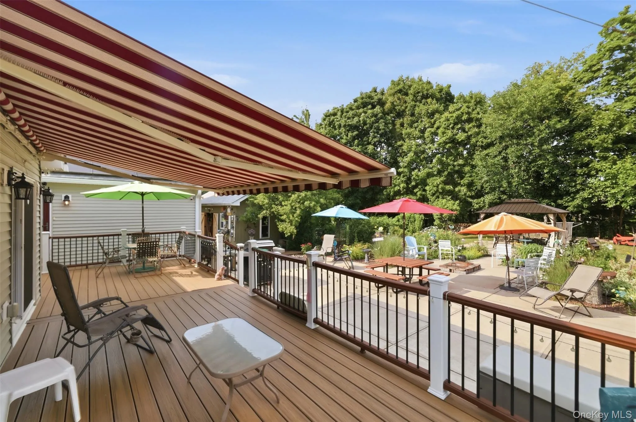 Expansive rear deck featuring a retractable striped awning, composite wood-finish decking, and black metal railings Expansive rear deck featuring a retractable striped awning, composite wood-finish decking, and black metal railings