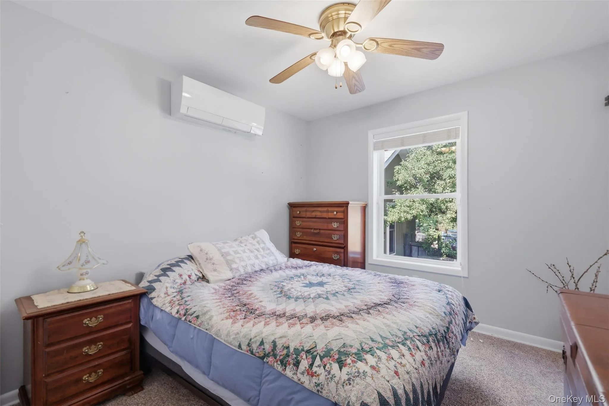 Interior room featuring light gray walls, a white-framed window, a ceiling fan with light fixture, and a wall-mounted mini-split unit Interior room featuring light gray walls, a white-framed window, a ceiling fan with light fixture, and a wall-mounted mini-split unit