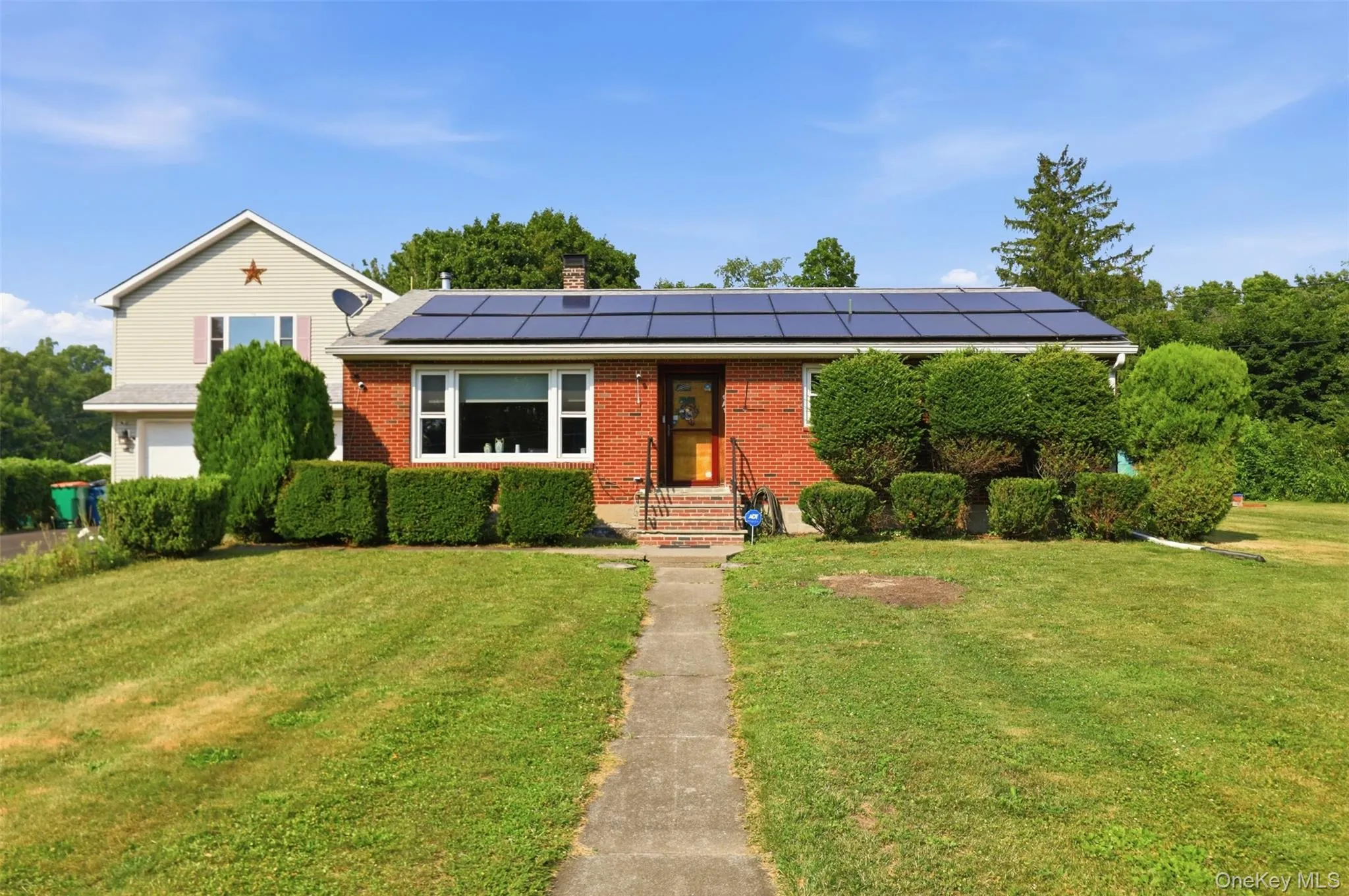 Brick facade home featuring solar panels and a landscaped front yard with a concrete walkway Brick facade home featuring solar panels and a landscaped front yard with a concrete walkway