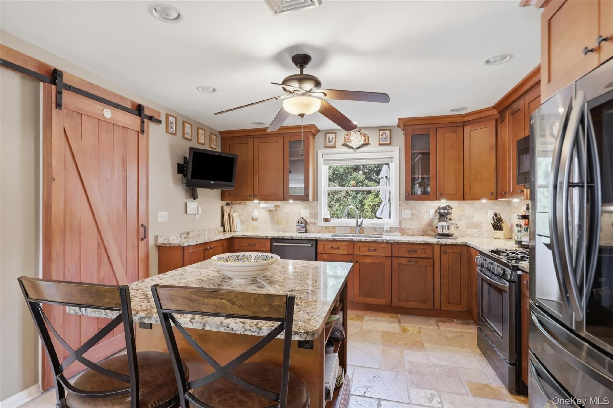 Kitchen featuring a large central island with a granite countertop, wood-finish cabinetry, stone tile flooring, and a barn door entry Kitchen featuring a large central island with a granite countertop, wood-finish cabinetry, stone tile flooring, and a barn door entry