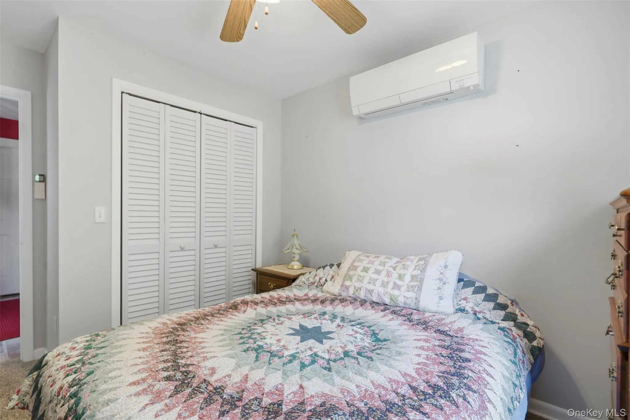 Bedroom featuring a ceiling fan, wall-mounted climate control unit, and louvered bifold closet doors Bedroom featuring a ceiling fan, wall-mounted climate control unit, and louvered bifold closet doors